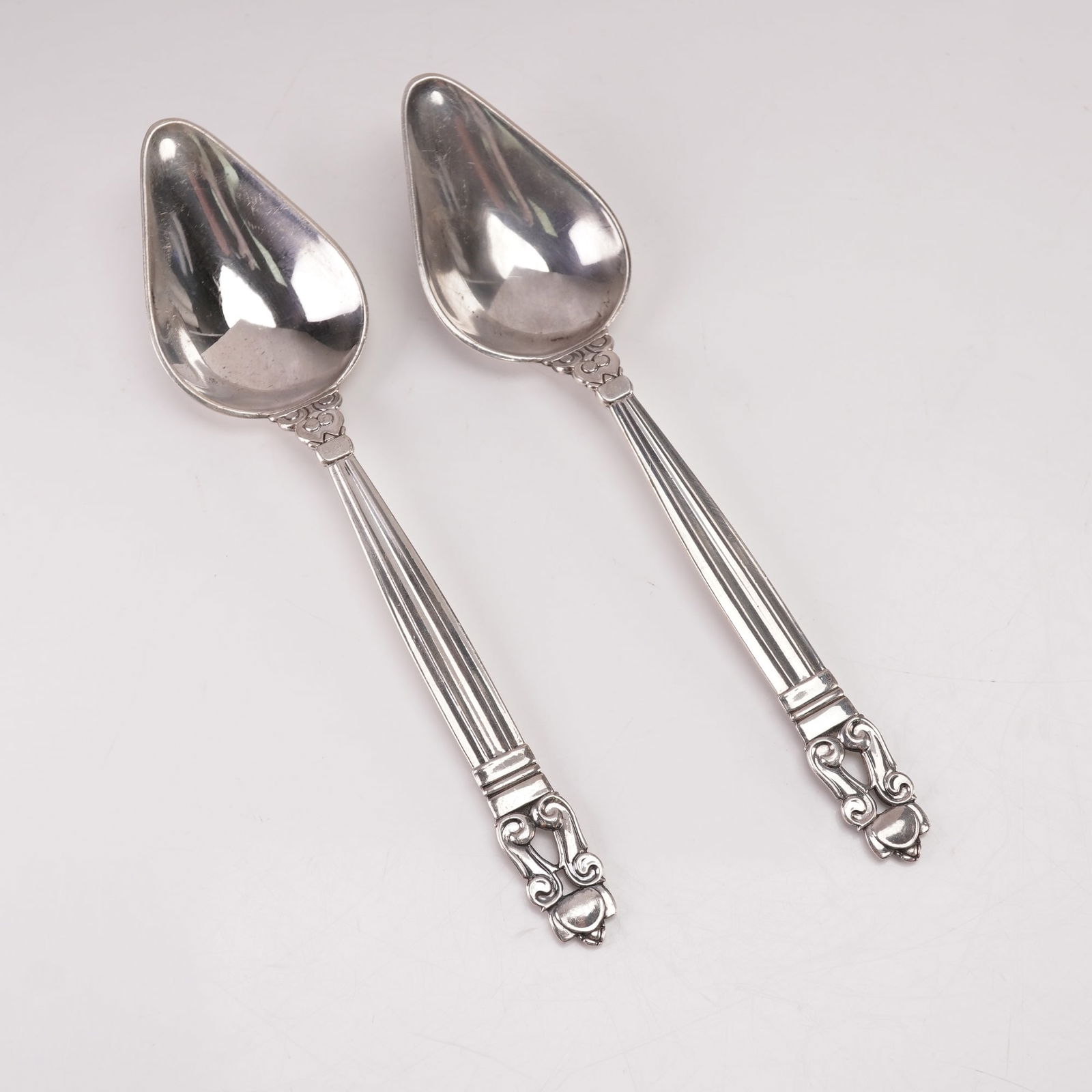 2pc Georg Jensen Sterling Silver Grapefruit Spoons, Acorn: This elegant two-piece set of Georg Jensen sterling silver grapefruit spoons features the renowned Acorn pattern, originally designed in 1915 by Johan Rohde. Each spoon displays the distinctive teardr