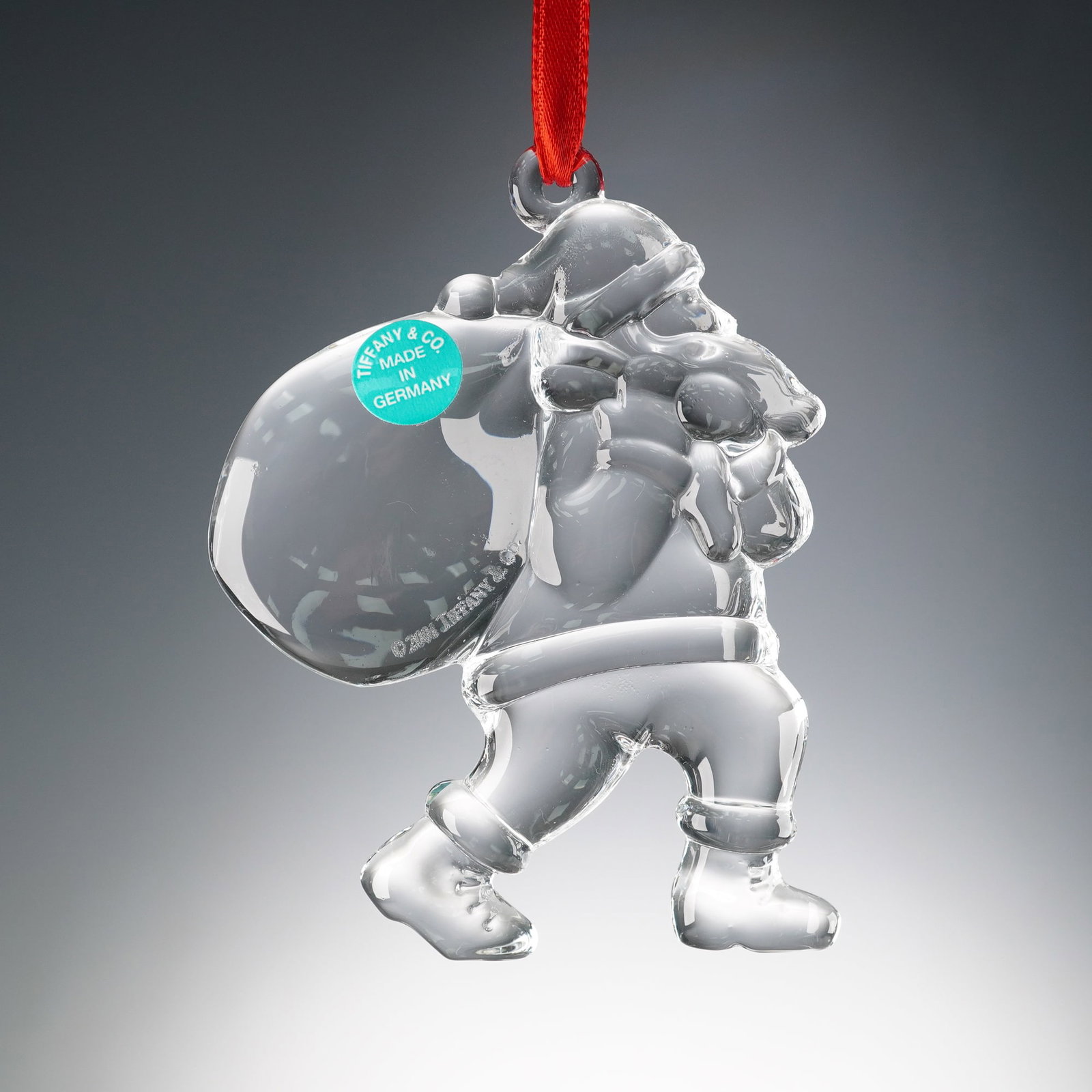 Tiffany & Co. Crystal Ornament, Santa with Bag: A Tiffany & Co. crystal ornament depicting Santa Claus carrying a large bag over his shoulder. This clear crystal design captures the festive holiday spirit with charming detail, complete with a red r