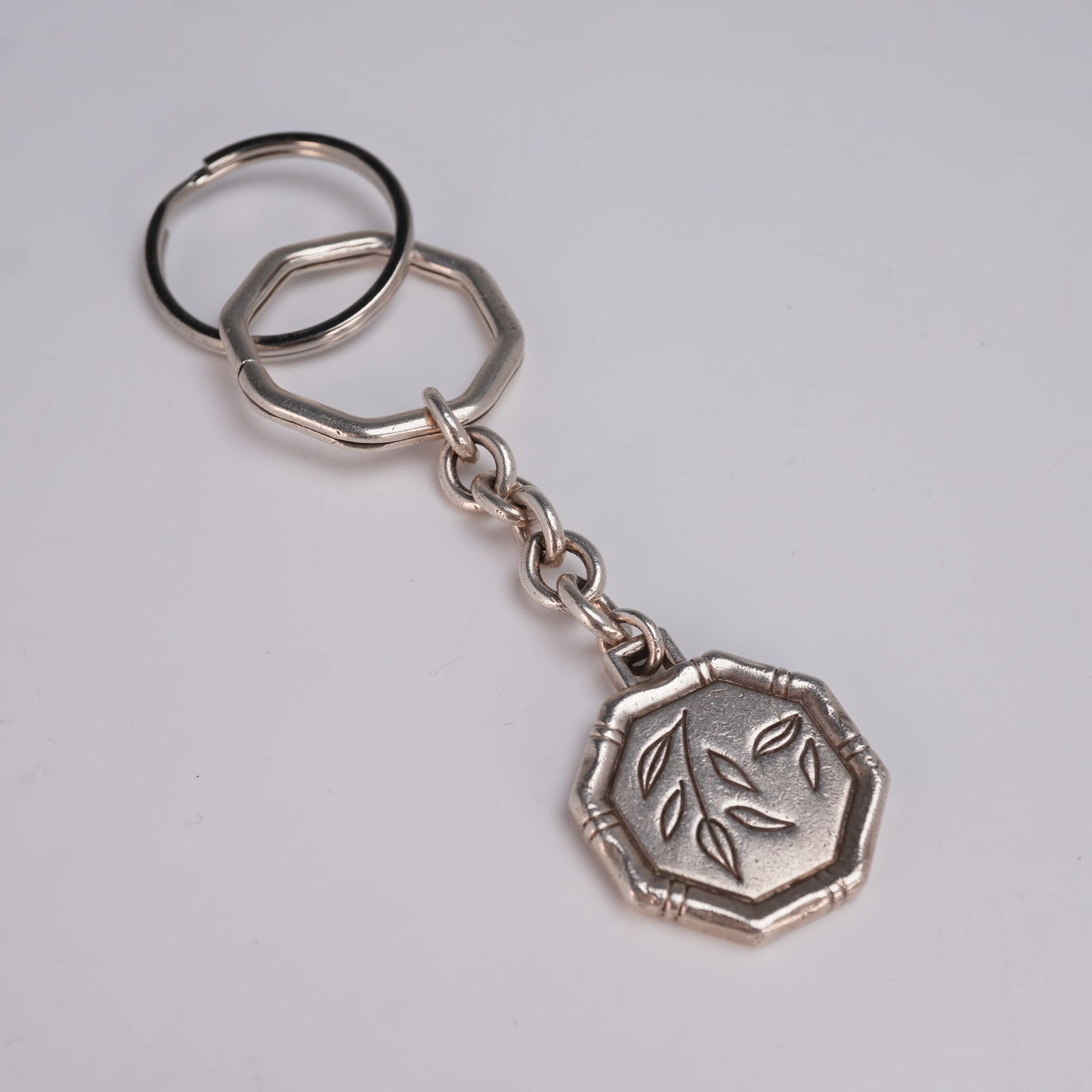 Tiffany & Co. Sterling Silver Leaf Motif Keychain: A Tiffany & Co. keychain crafted in sterling silver, featuring an octagonal fob engraved with a leaf design and framed with bamboo-style edging. The reverse is stamped Tiffany & Co. 925. Complete with