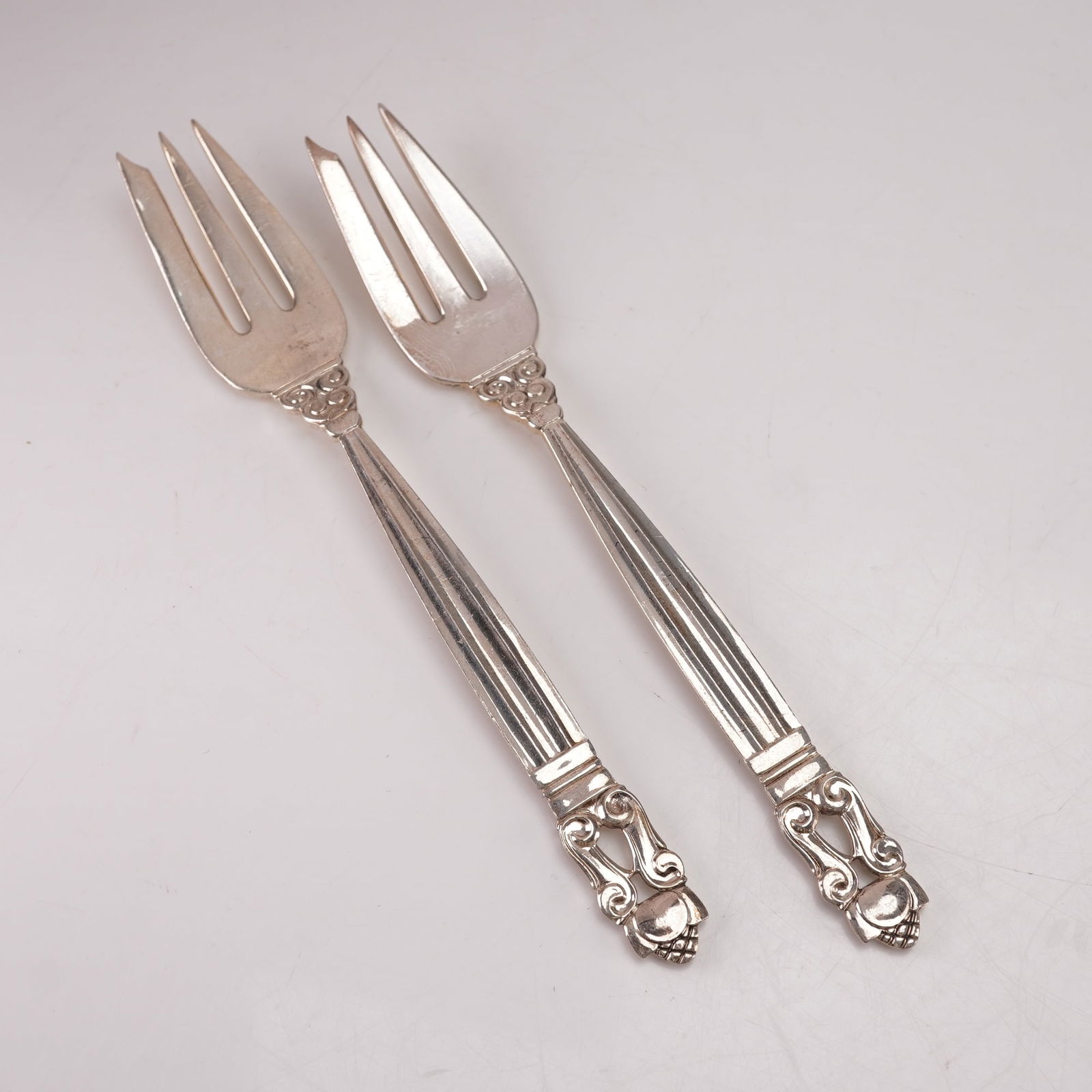 2pc Georg Jensen Sterling Silver Pastry Forks, Acorn: A two-piece set of Georg Jensen sterling silver pastry forks in the Acorn pattern, designed by Johan Rohde in 1915. Marked Georg Jensen Sterling Denmark. The pattern features a tapered fluted handle l