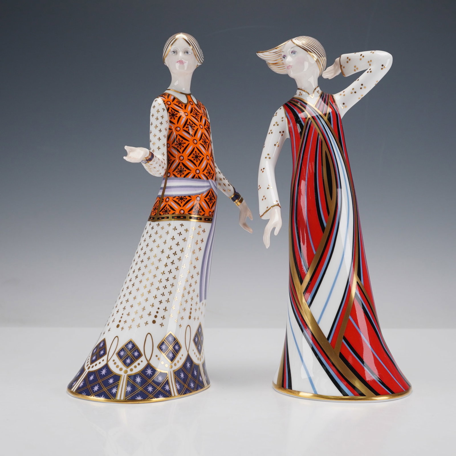2pc Royal Crown Derby Classic Collection Figurines, Athena & Penelope: This elegant bone china pair showcases the refined artistry of Royal Crown Derby, featuring two elongated female figures with stylized, Art Deco-inspired designs. "Athena" wears a striking orange and 