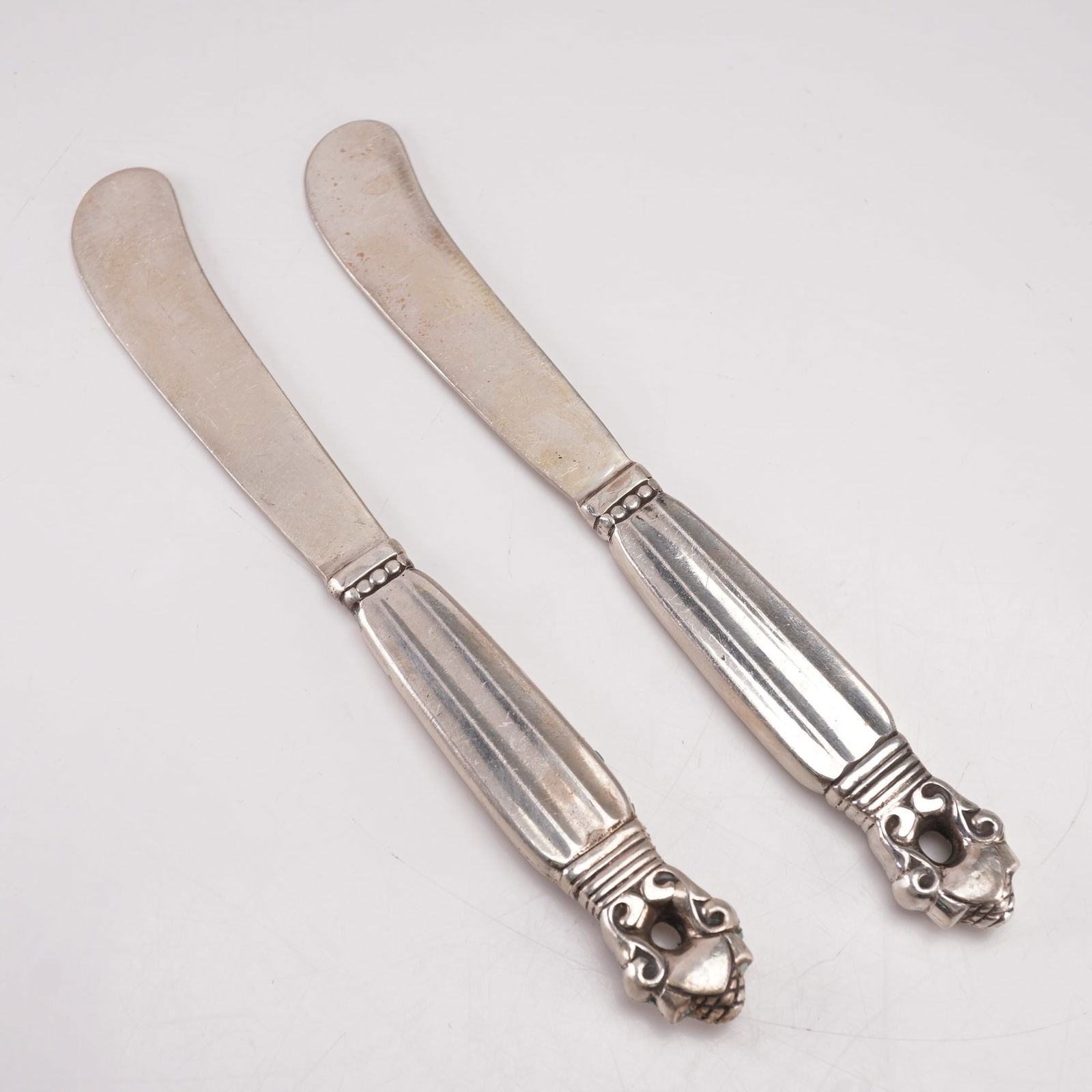 2pc Georg Jensen Sterling Silver Paddle Butter Spreaders, Acorn: A two-piece lot of Georg Jensen sterling silver hollow handle paddle butter spreaders in the Acorn pattern, designed by Johan Rohde in 1915. Each marked Georg Jensen Sterling Denmark. The pattern feat