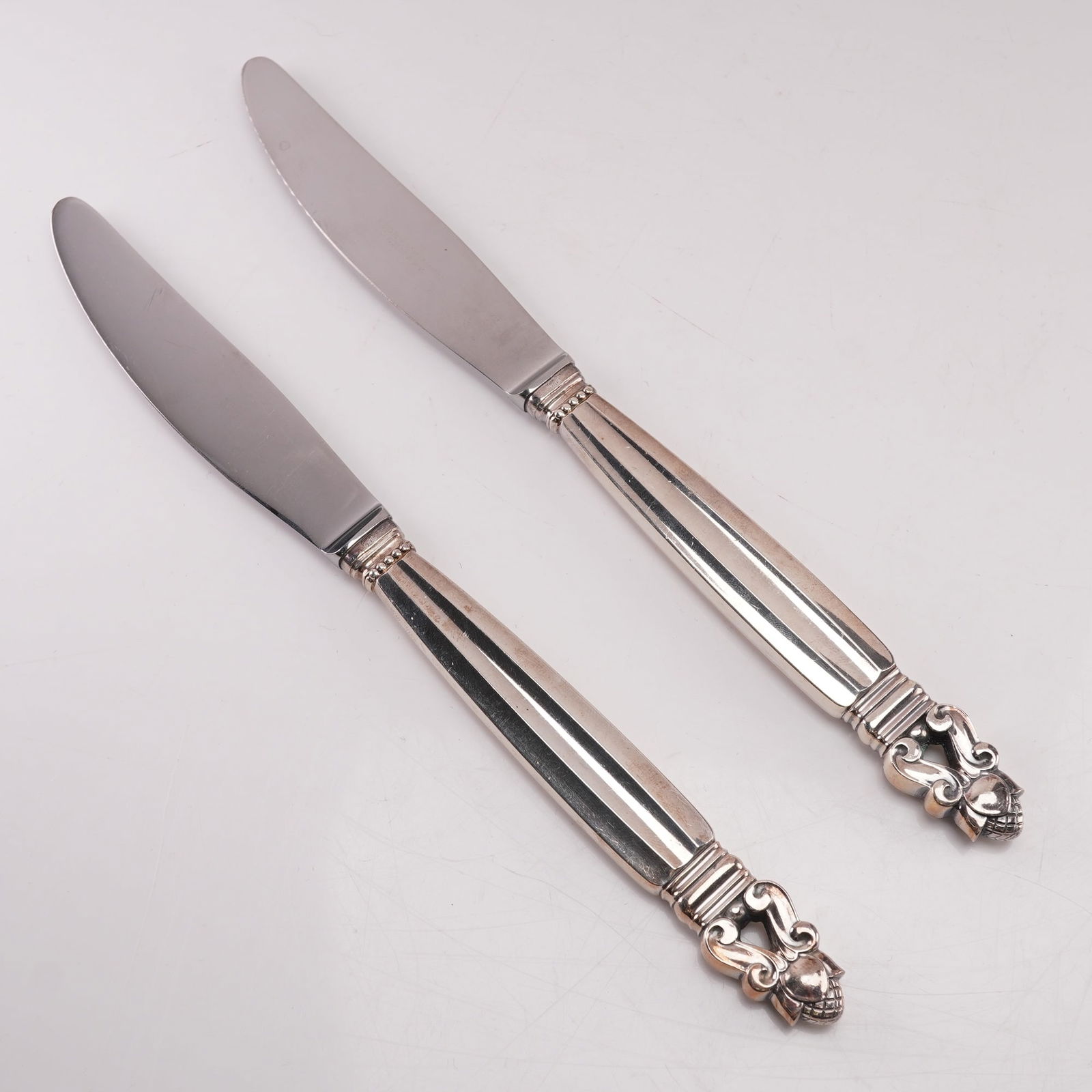 2pc Georg Jensen Sterling Silver Stainless Steel Dinner Knives, Acorn: A two-piece lot of Georg Jensen dinner knives in the Acorn pattern, designed by Johan Rohde in 1915. Each knife features a sterling silver handle marked Sterling Denmark with the Georg Jensen hallmark