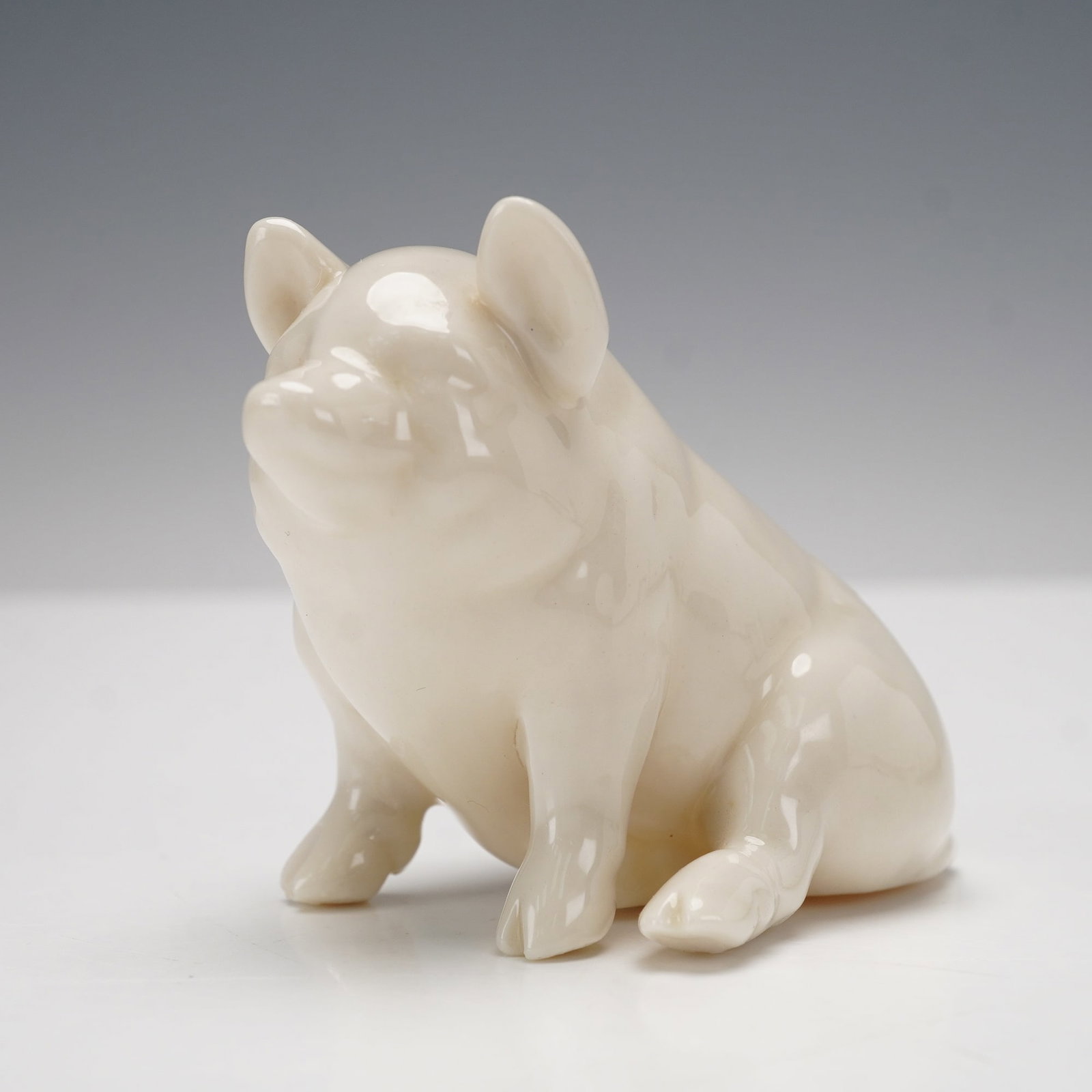 Belleek Porcelain Figurine, Sitting Pig: Charming Irish Belleek porcelain figurine depicting a seated pig in a glossy cream finish. The smooth, delicate glaze accentuates the naturalistic form and gentle facial expression. Marked on the unde