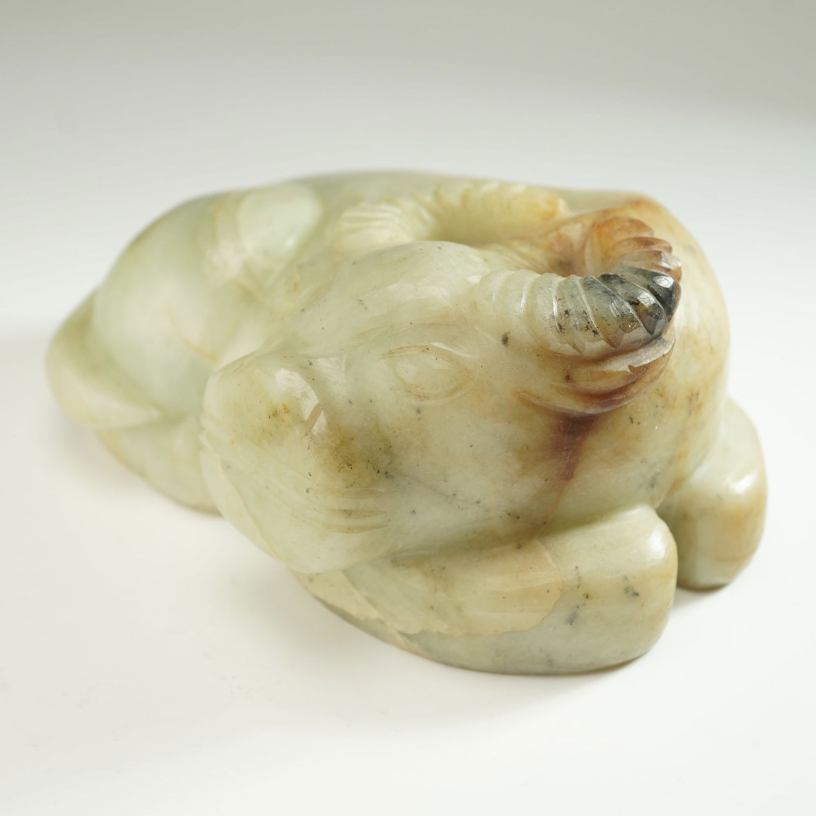Chinese Recumbent Water Buffalo Jade Carved Figurine: Stone carving depicting a recumbent water buffalo in a resting position, finely carved with defined facial features, curled horns, and a smooth, polished surface. The stone exhibits natural variations