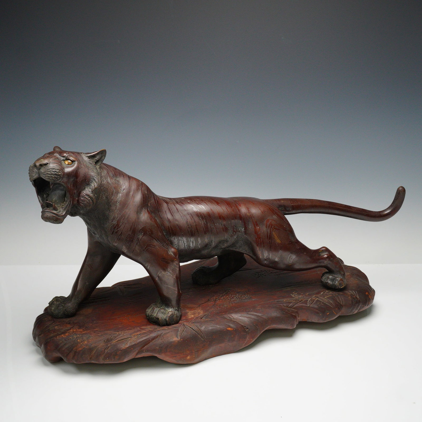 Japanese Meiji Period Bronze Tiger Sculpture on Carved Wood Base: A finely cast Japanese bronze sculpture of a prowling tiger, dating to the Meiji period (1868 -1912). The tiger is depicted in mid-stride with mouth open in a ferocious roar, showing superb detailing 