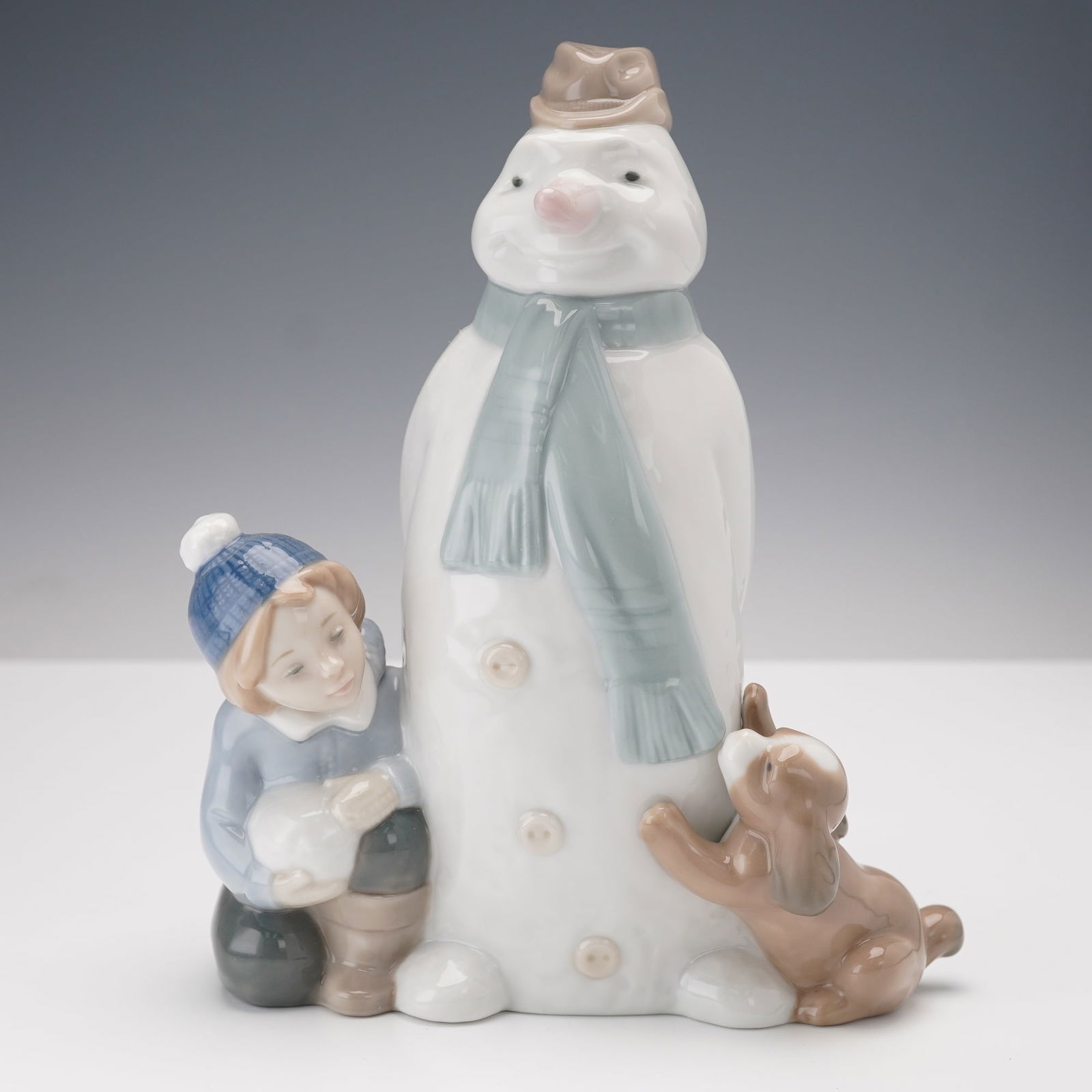 Nao by Lladro Porcelain Figurine Snowman with Child and Dog 1438: This Nao by Lladro porcelain figurine, model 1438, features a snowman, a child with a snowball, and a dog. The piece is crafted in soft pastel tones and detailed with a scarf and hat on the snowman. I