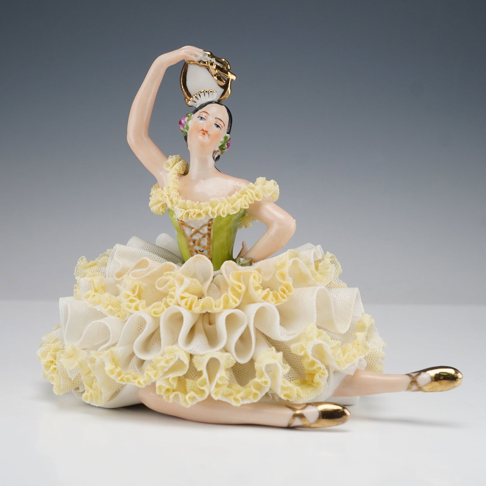 WR Dresden Style Lace Figurine Spanish Dancer with Tambourine: A beautifully detailed lace figurine depicting a Spanish dancer seated gracefully with one arm raised holding a tambourine. She is dressed in a layered gown of yellow and white porcelain lace with a g