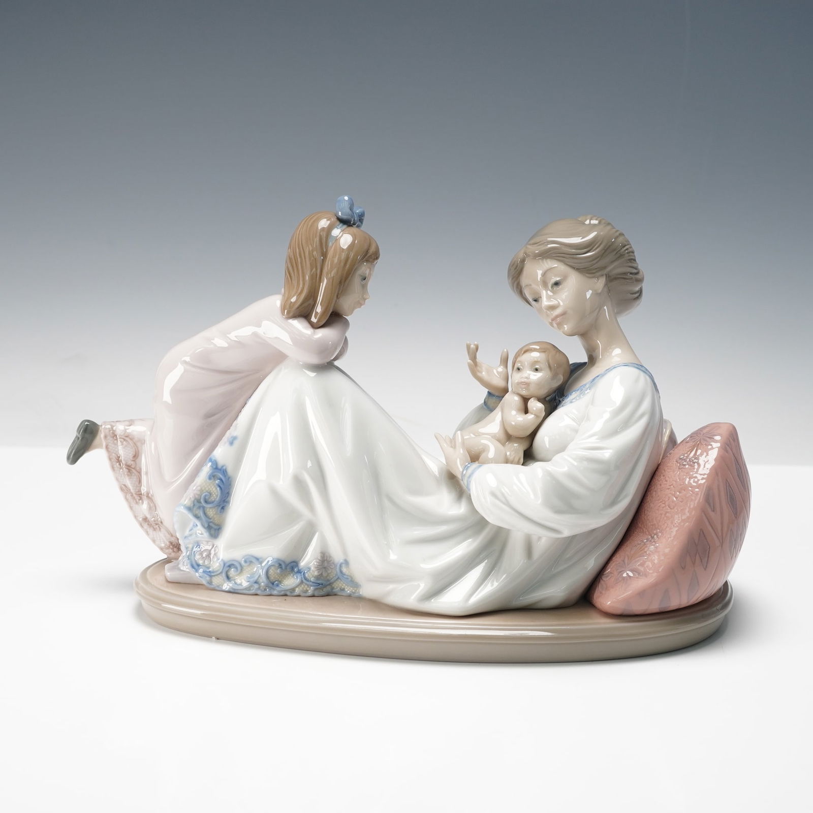 Lladro Porcelain Figurine, Latest Addition 1001606: Glossy porcelain figurine titled Latest Addition, sculpted by Jose Puche and issued in 1989, depicting a mother with an infant and young child. Soft pastel tones and delicate detail highlight classic