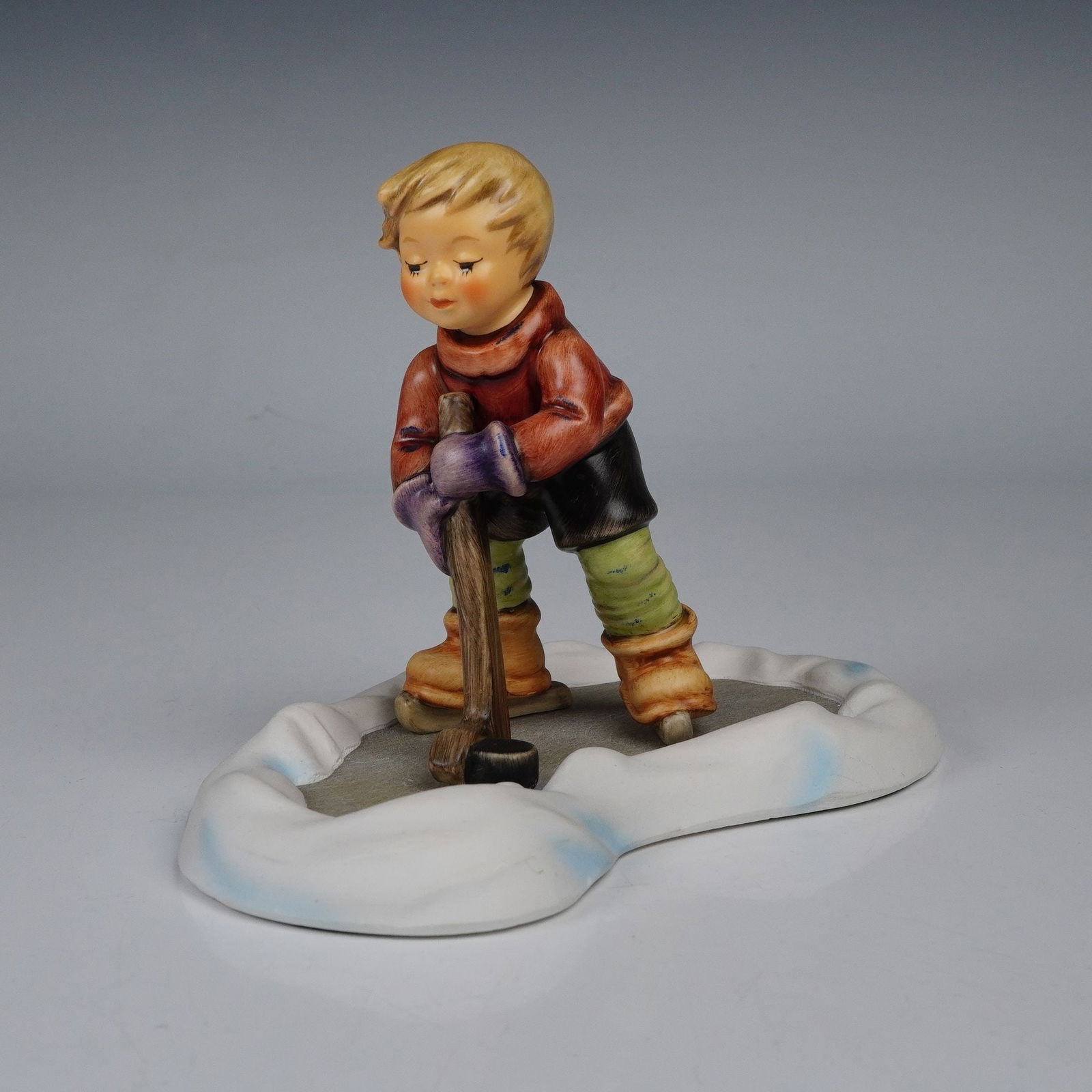 Goebel Hummel Porcelain Figurine, Hockey Player: Charming Goebel M.I. Hummel porcelain figurine titled Hockey Player, featuring a young boy dressed in winter attire, skating on a frozen pond with a hockey stick in hand. Expertly hand-painted with fi