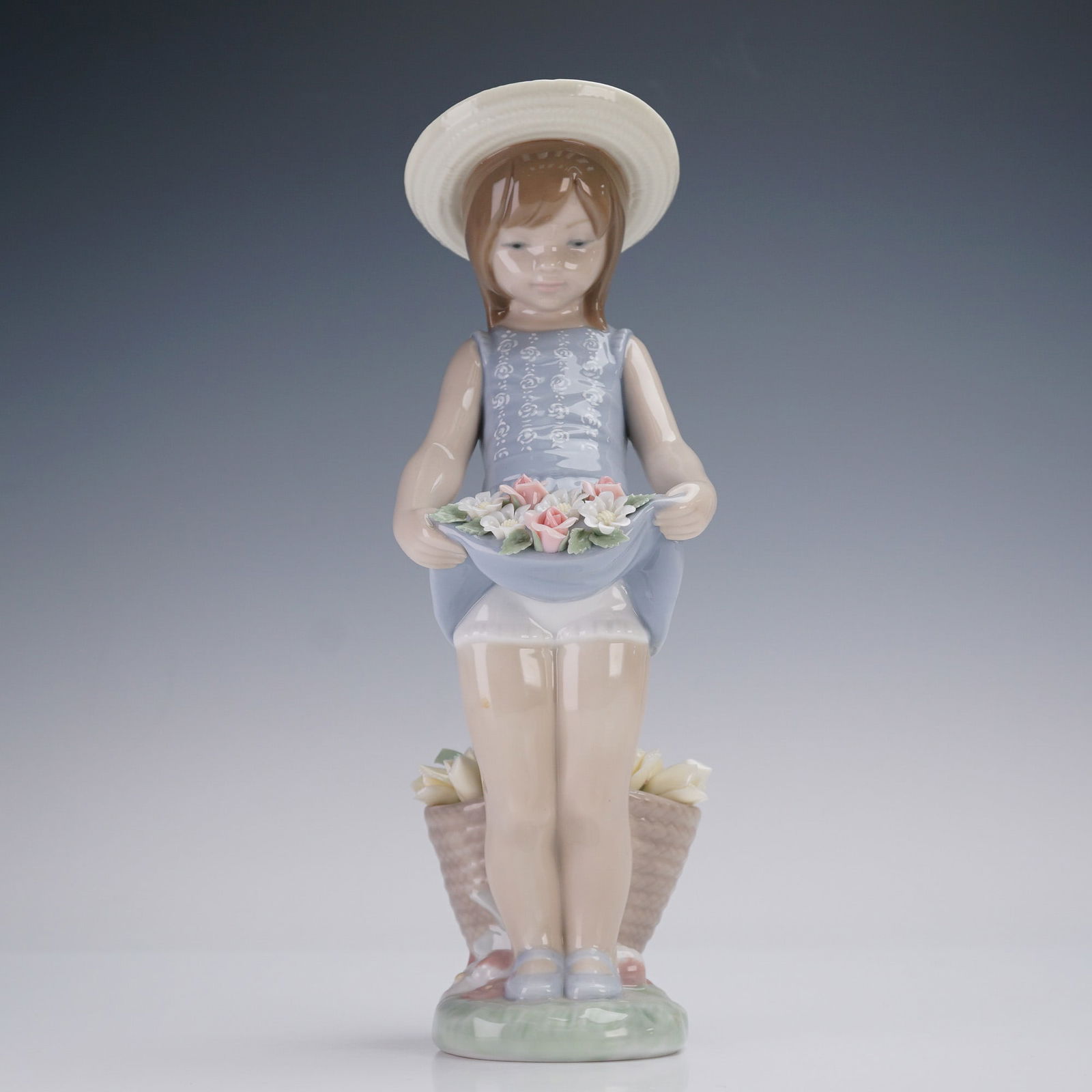 Lladro Porcelain Figurine, Flowers on the Lap 1001284: This Lladro porcelain figurine titled Flowers on the Lap shows a young girl in a soft blue dress and wide hat holding delicate pink and white flowers in her lifted skirt. A woven basket full of blooms