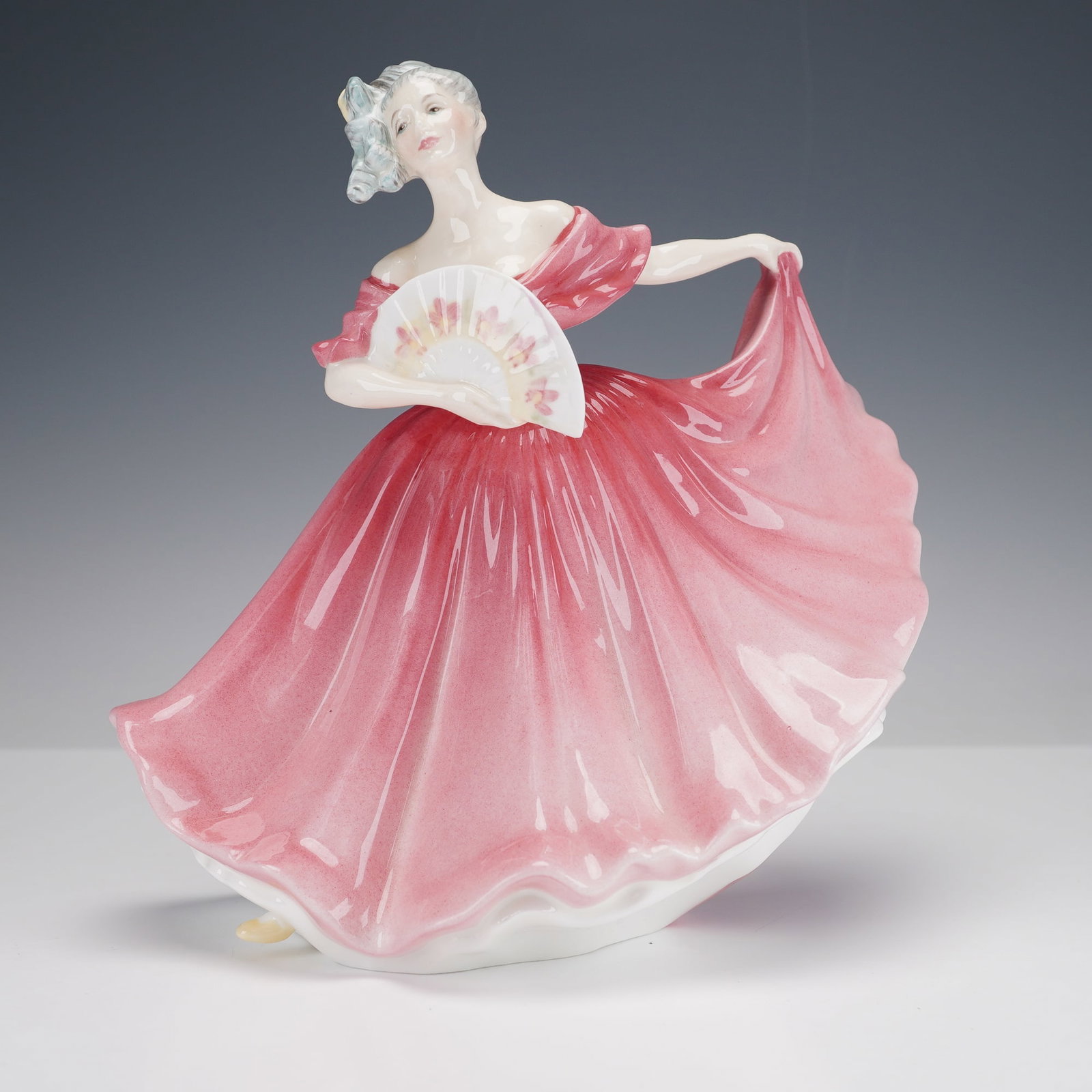 Royal Doulton Bone China Figurine, Elaine HN3307: This elegant hand-decorated figure depicts a graceful woman in a flowing rose-colored gown holding a floral fan, her head turned in a poised and serene expression. The underside bears the Royal Doulto