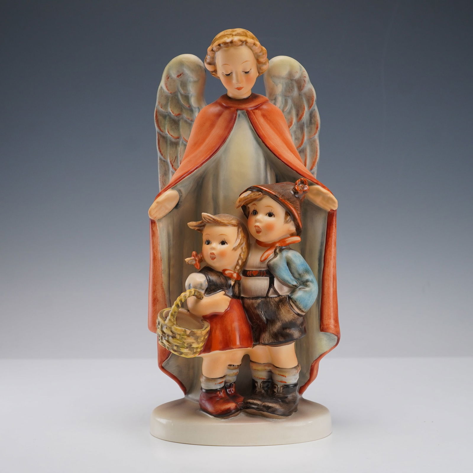 Goebel Hummel Figurine, Heavenly Protection: Goebel porcelain Hummel figurine titled Heavenly Protection. The piece depicts an angel spreading its wings protectively over two children, one holding a basket. Hand-painted in traditional soft hues