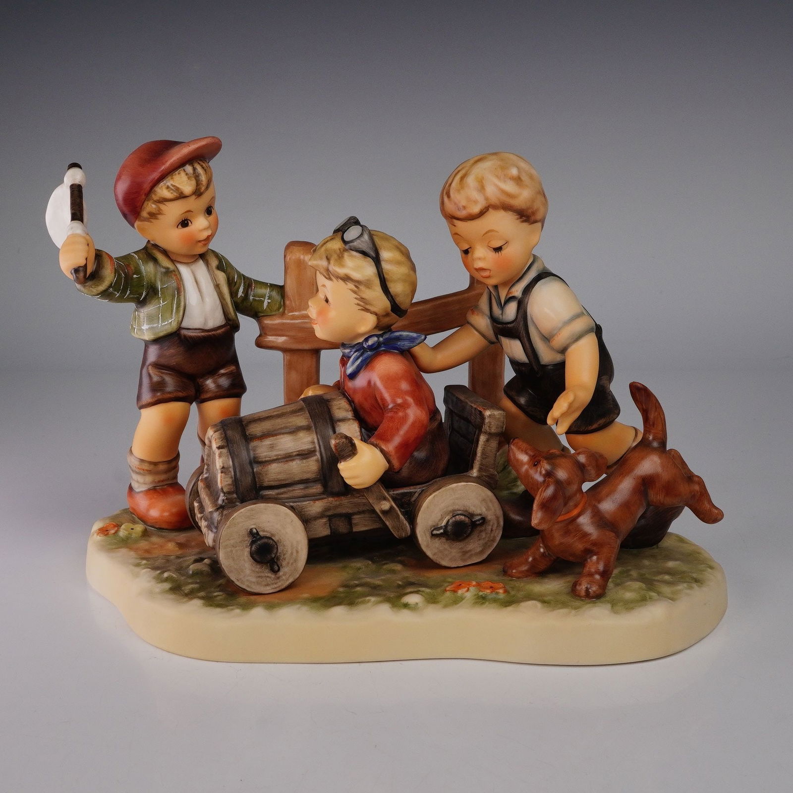 Goebel Hummel Moments in Time Figurine, Soapbox Derby: From the Moments in Time series, issued in 2002. This charming hand-painted porcelain sculpture depicts three boys and a dog enthusiastically engaged in a playful soapbox derby race, with one child st