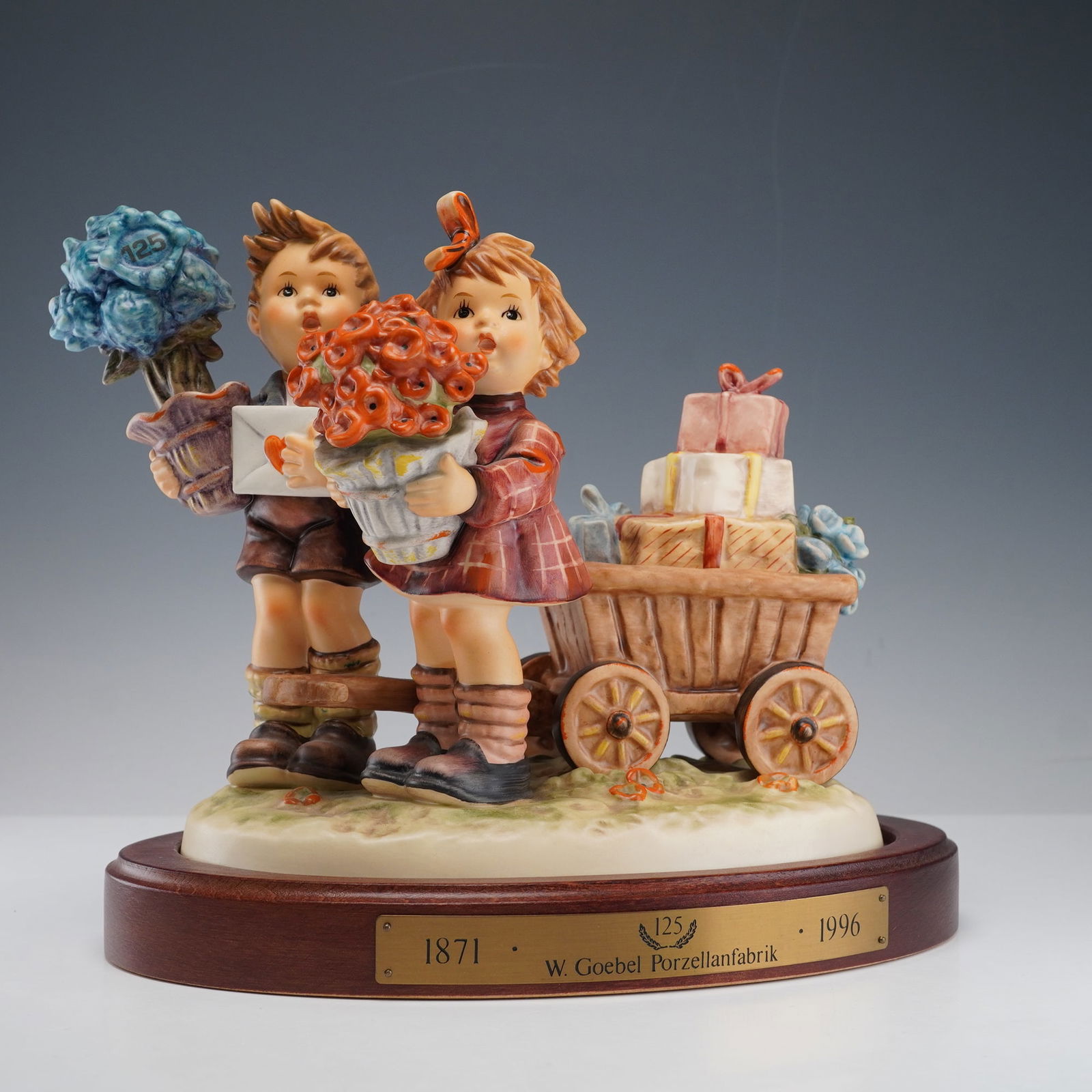 2pc Goebel Hummel Figurine, Loves Bounty with Base: This Goebel Hummel porcelain figurine titled Loves Bounty was created to commemorate the 125th anniversary of the W. Goebel Porzellanfabrik in 1996. It captures two cheerful children standing beside a