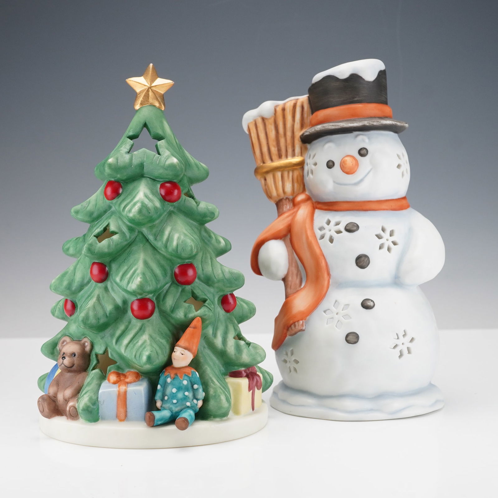 2pc Goebel Christmas Candle Tea Lights, Tree and Snowman: Duo of Goebel porcelain Christmas candle tea lights including a decorated Christmas tree with red ornaments, along with a snowman holding a broom and wearing a black hat and orange scarf. Both pieces