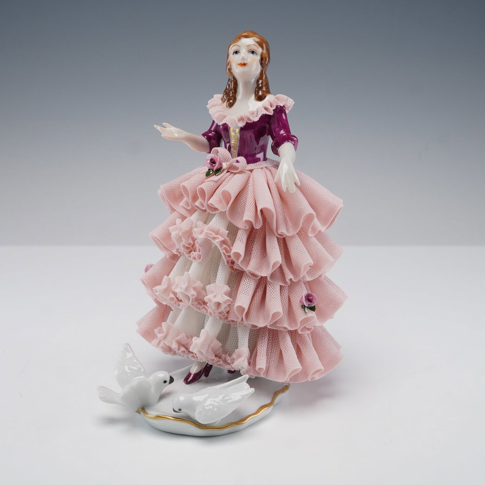 Dresden Porcelain Pink Lace Women and Doves Figurine: This delicate Dresden porcelain figurine portrays a graceful woman in an elegant tiered pink lace dress with a deep plum bodice and ruffled collar. Intricate details include soft curls framing her fac