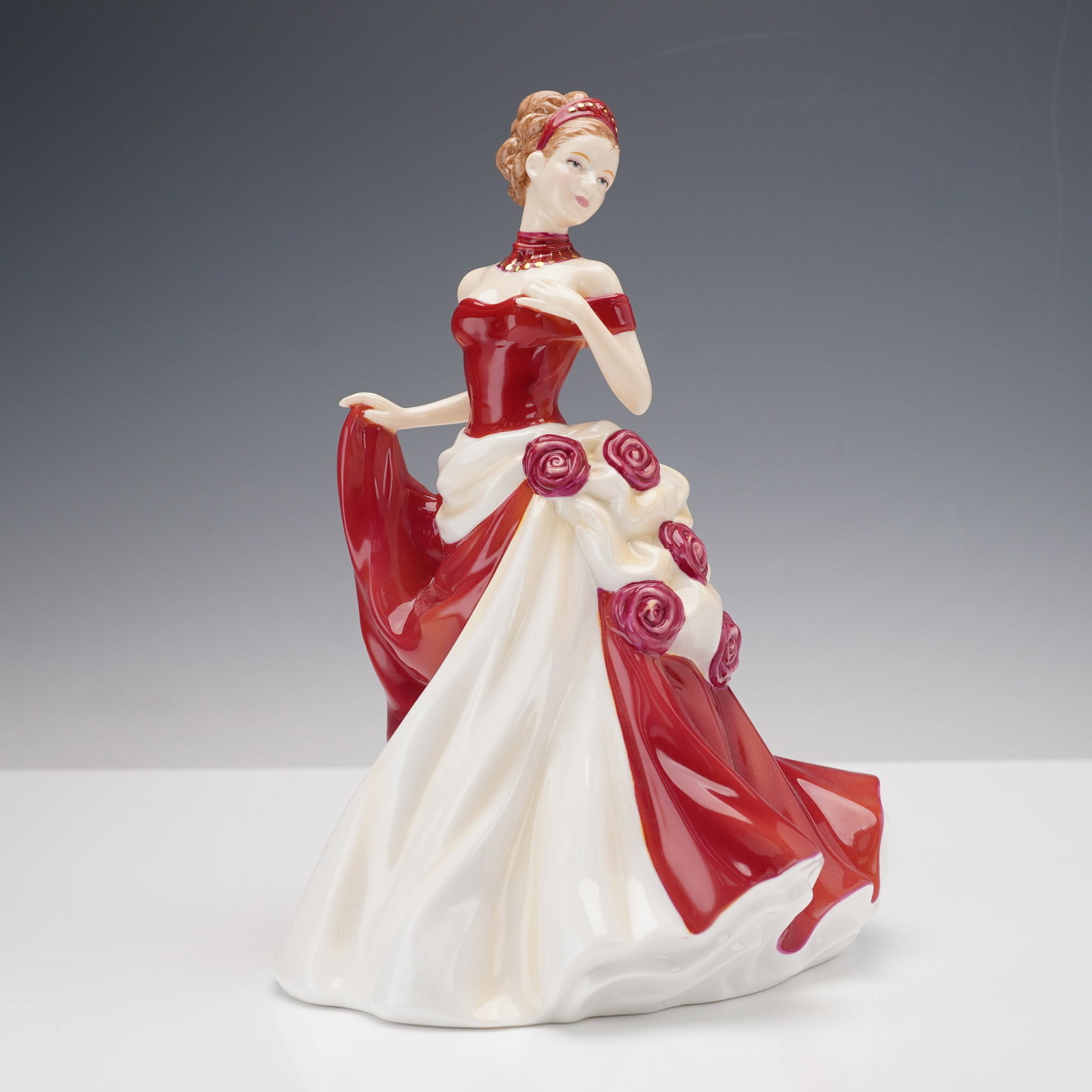 Royal Doulton Pretty Ladies Bone China Figurine, From The Heart HN5143: A finely crafted hand-decorated porcelain figure depicting an elegant lady in a flowing red and white gown adorned with rose accents. Her graceful pose and detailed expression exemplify the charm and 