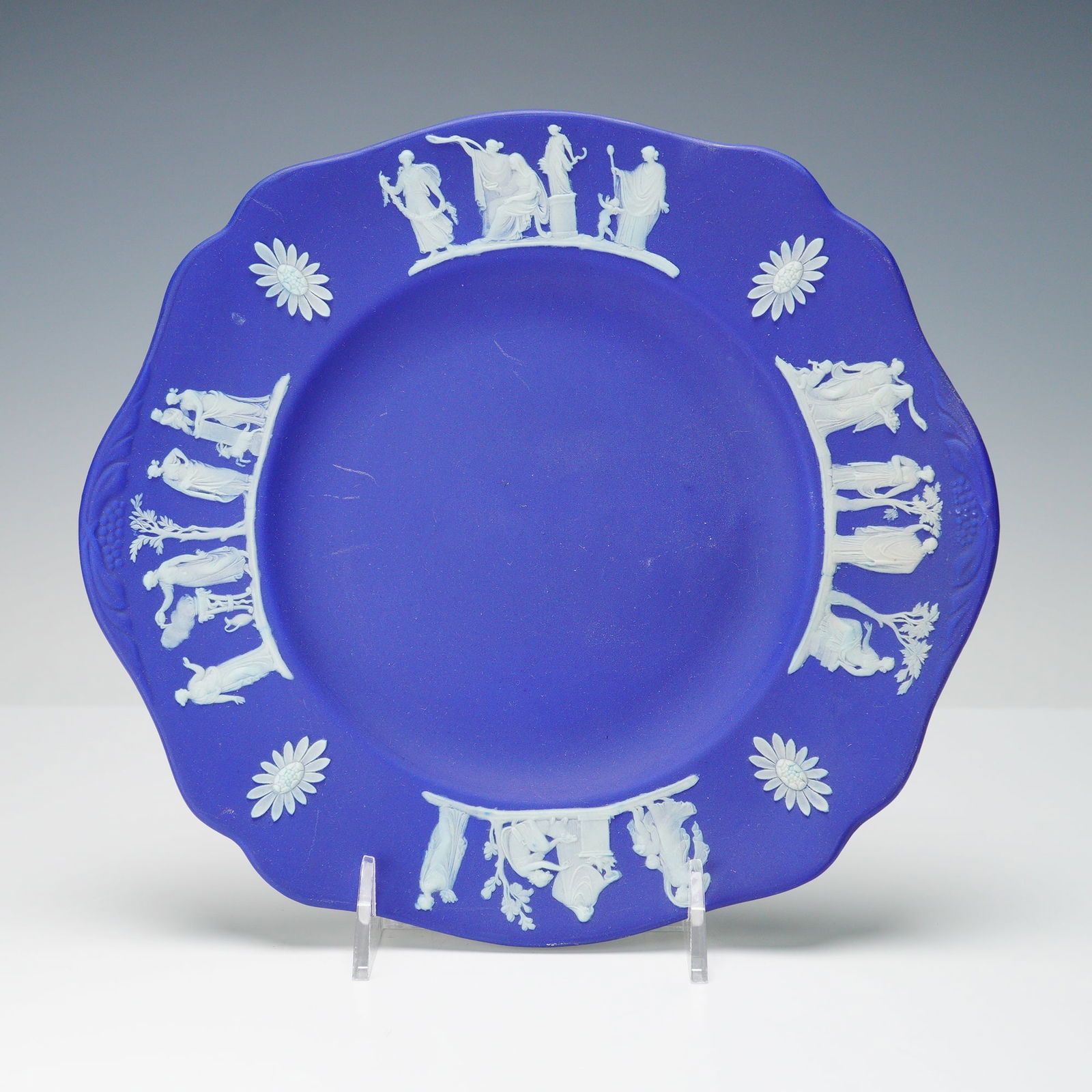 Wedgwood Blue Jasperware Relief Plate: A fine example of Wedgwood's iconic jasperware, this cobalt blue plate is adorned with classical white relief scenes depicting figures from Greco-Roman mythology in procession, alternating with floral