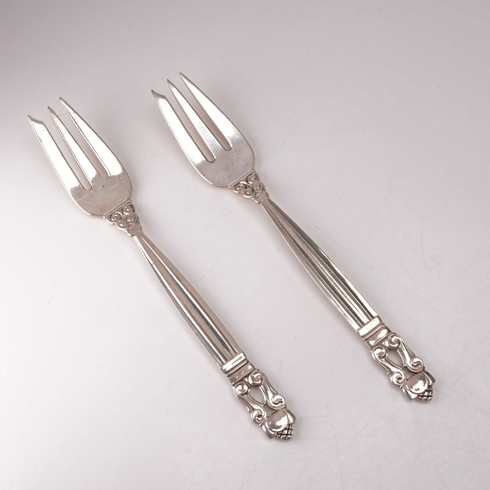 2pc Georg Jensen Sterling Silver Pastry Forks, Acorn: A two-piece lot of Georg Jensen sterling silver pastry forks in the Acorn pattern, designed by Johan Rohde in 1915. Marked Georg Jensen Sterling Denmark. The pattern features a tapered fluted handle l