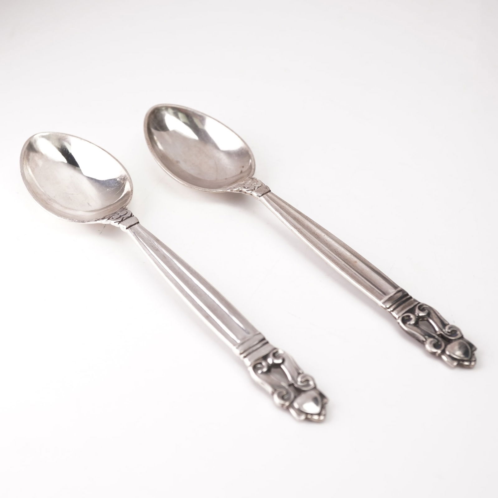 Pair of Georg Jensen Sterling Silver Fruit Spoons, Acorn: A two-piece lot of Georg Jensen sterling silver fruit spoons in the Acorn pattern, designed by Johan Rohde and introduced in 1915. Each spoon features a gently rounded bowl and a tapered handle with f