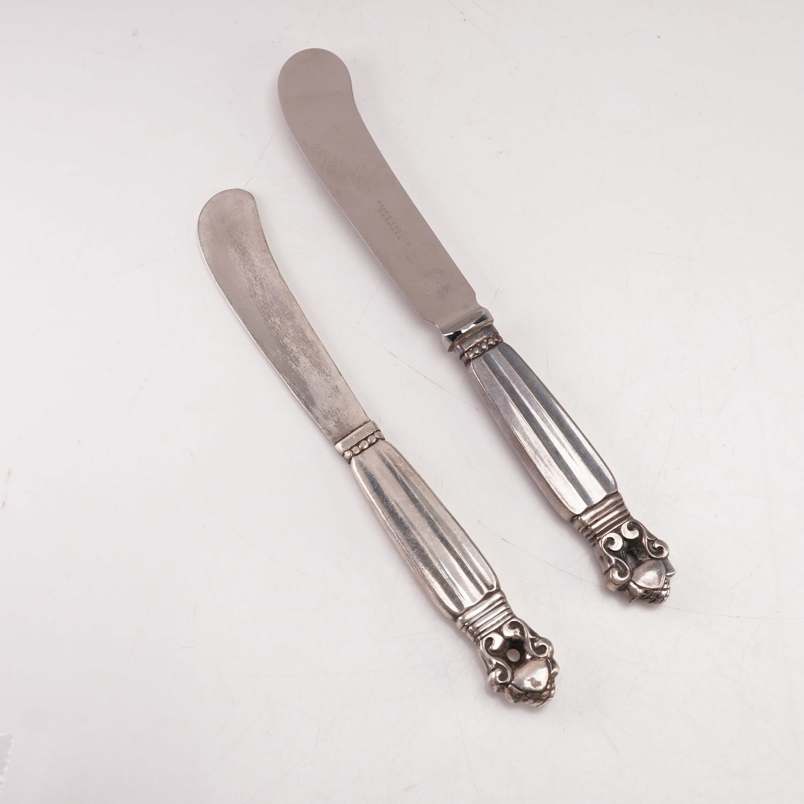 2pc Georg Jensen Sterling Silver Paddle Butter Spreaders, Acorn: A two-piece lot of Georg Jensen sterling silver hollow handle paddle butter spreaders in the Acorn pattern, designed by Johan Rohde in 1915. Each marked Georg Jensen Sterling Denmark. The pattern feat