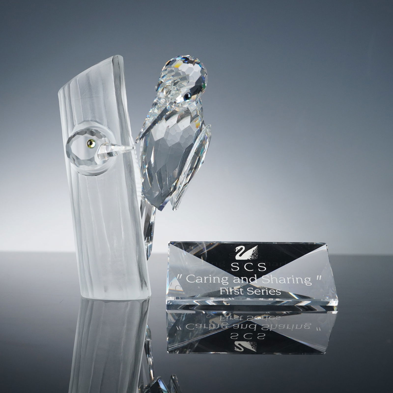 2pc Swarovski Caring & Sharing Crystal Figurine & Plaque, Woodpeckers: Exquisitely crafted crystal sculpture depicting two woodpeckers perched on a frosted crystal tree trunk, designed as part of the Swarovski Crystal Society (SCS) First Series. Includes accompanying cle