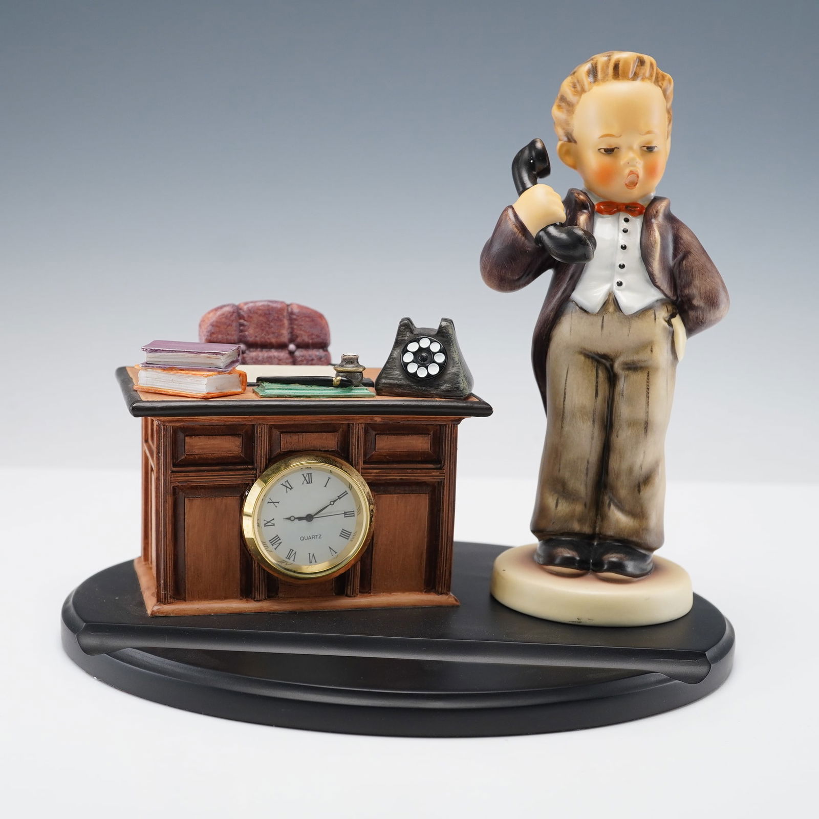 2pc Goebel Hummel Figurine and Base, Hello and Just Business: This Goebel Hummel set pairs the figurine Hello with the Hummelscape base Just Business to create a lively office scene. The boy stands with a serious expression as he speaks on a classic black teleph