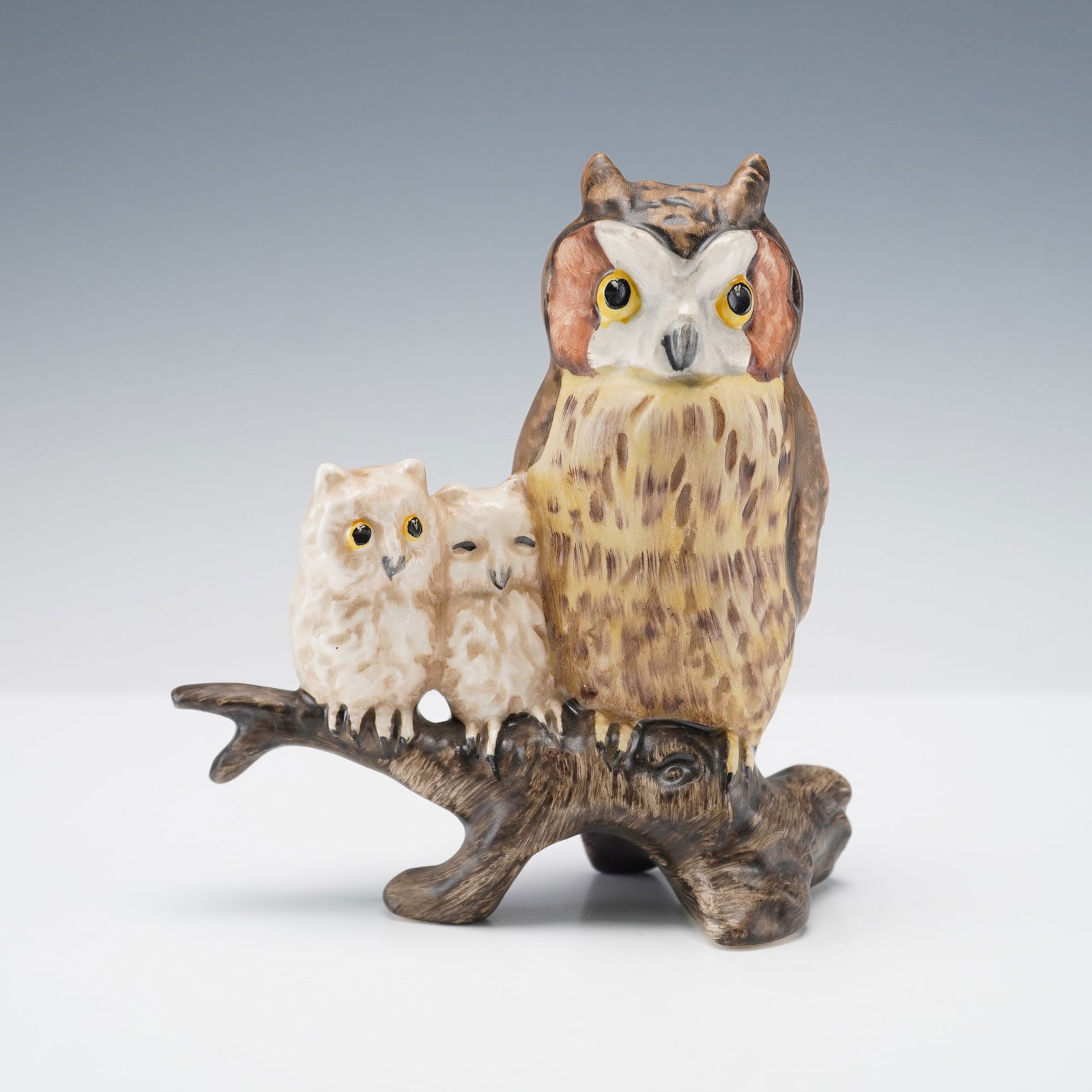 Goebel Figurine, Owls on Branch: Goebel porcelain figurine depicting a family of owls perched on a tree branch, featuring a large owl with two owlets beside it. Hand-painted in natural tones of brown, cream, and yellow with detailed