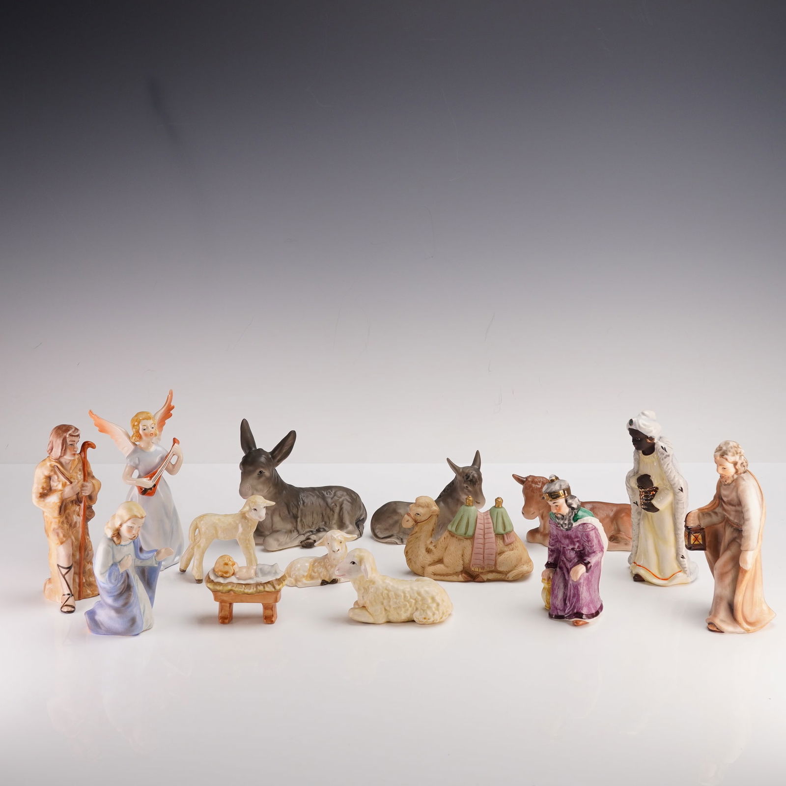 14 pc Goebel Hummel Nativity Figurines: A finely crafted porcelain nativity collection made in West Germany by Goebel, featuring hand-painted figures depicting the traditional Christmas scene. The set includes Mary kneeling beside the infan