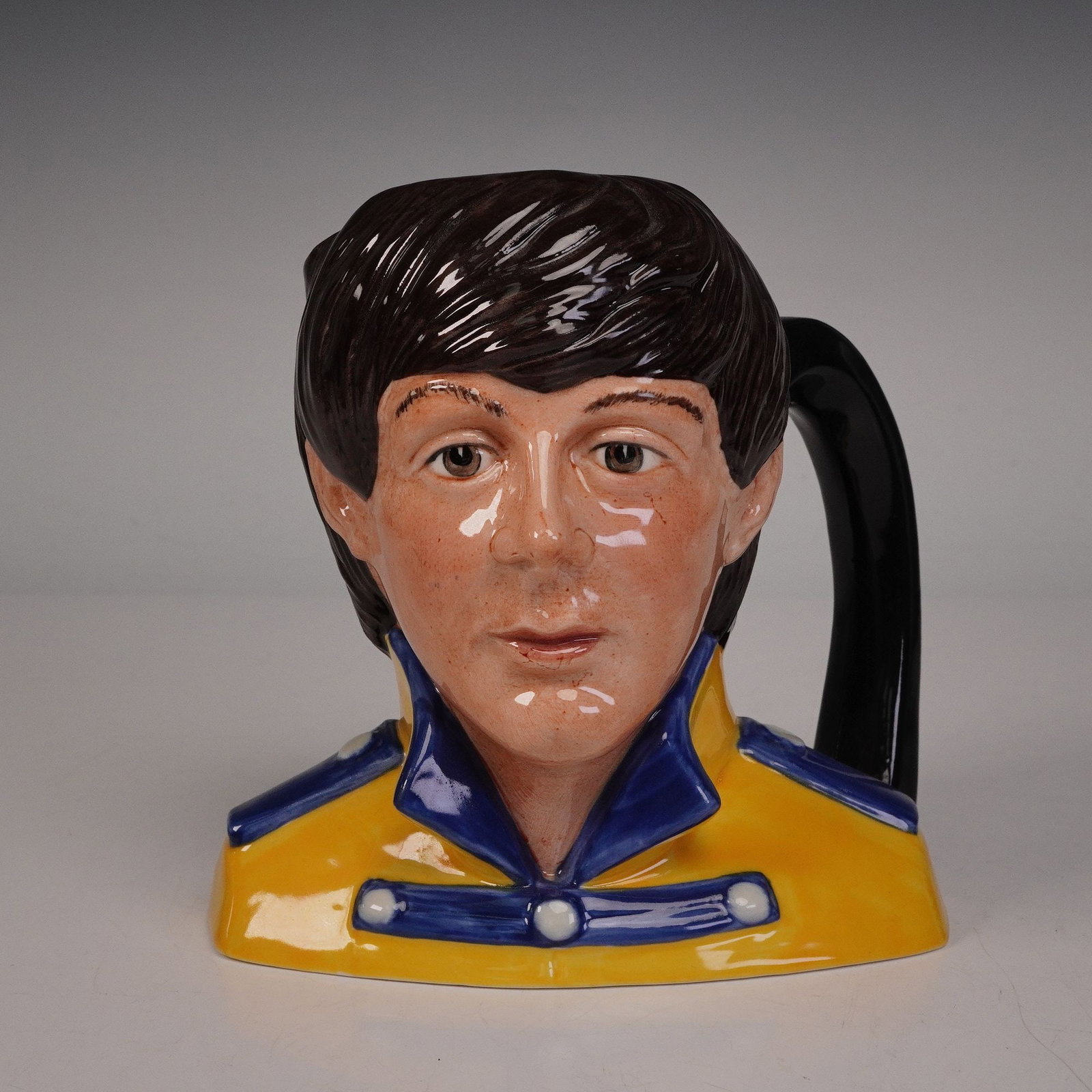 Royal Doulton The Beatles Character Jug, Paul McCartney D6724 Signed: A finely crafted ceramic character jug depicting musician Paul McCartney, produced as part of The Beatles collection. The piece portrays McCartney in a vivid yellow and blue uniform inspired by the ic