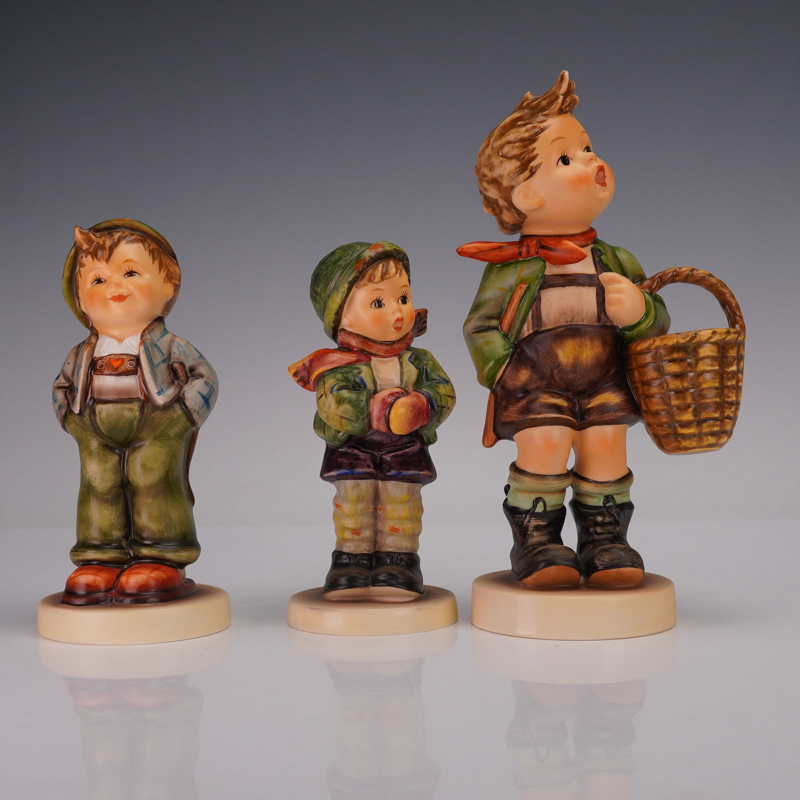 3pc Goebel Hummel Young Boy Figurines: A set of 3 Goebel Hummel porcelain figurines, each depicting a young boy. One shows a boy with hands in his pockets, marked on the base "Exclusive Edition 1989/90 M.I. Hummel Club." Another depicts a