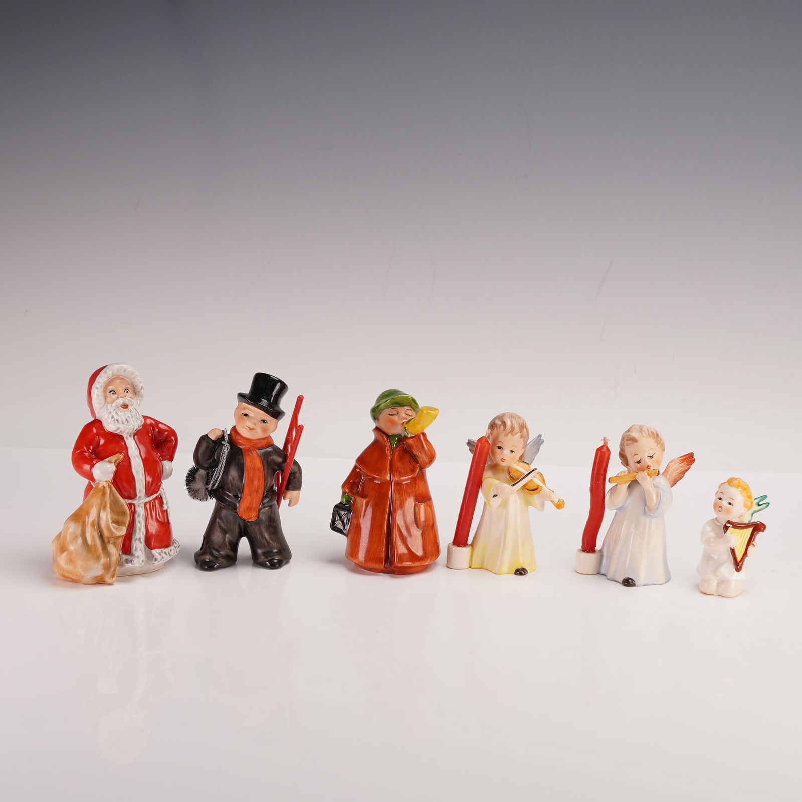 6pc Goebel Hummel Winter Themed Figurines: This six piece Goebel Hummel figurine set features a charming collection of holiday and angelic figures. It includes Santa Claus with a sack, a cheerful chimney sweep with a ladder and brush, and a to