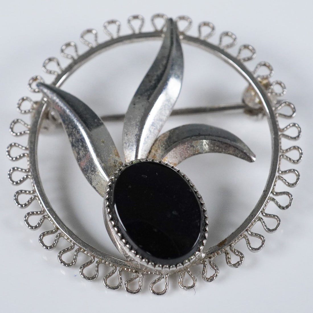 Sterling Silver Floral Brooch with Black Onyx: This petite sterling silver brooch features an abstract floral motif with three gracefully arched leaves surrounding a polished oval cabochon of black onyx. The stylized bloom is framed by an openwork