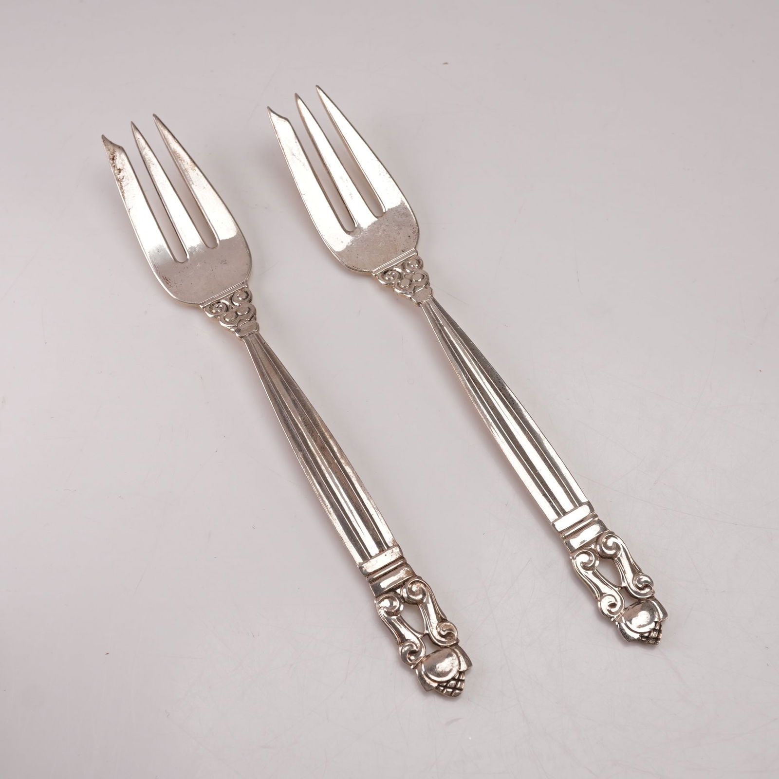 2pc Georg Jensen Sterling Silver Pastry Forks, Acorn: A two-piece lot of Georg Jensen sterling silver pastry forks in the Acorn pattern, designed by Johan Rohde in 1915. Marked Georg Jensen Sterling Denmark. The pattern features a tapered fluted handle l