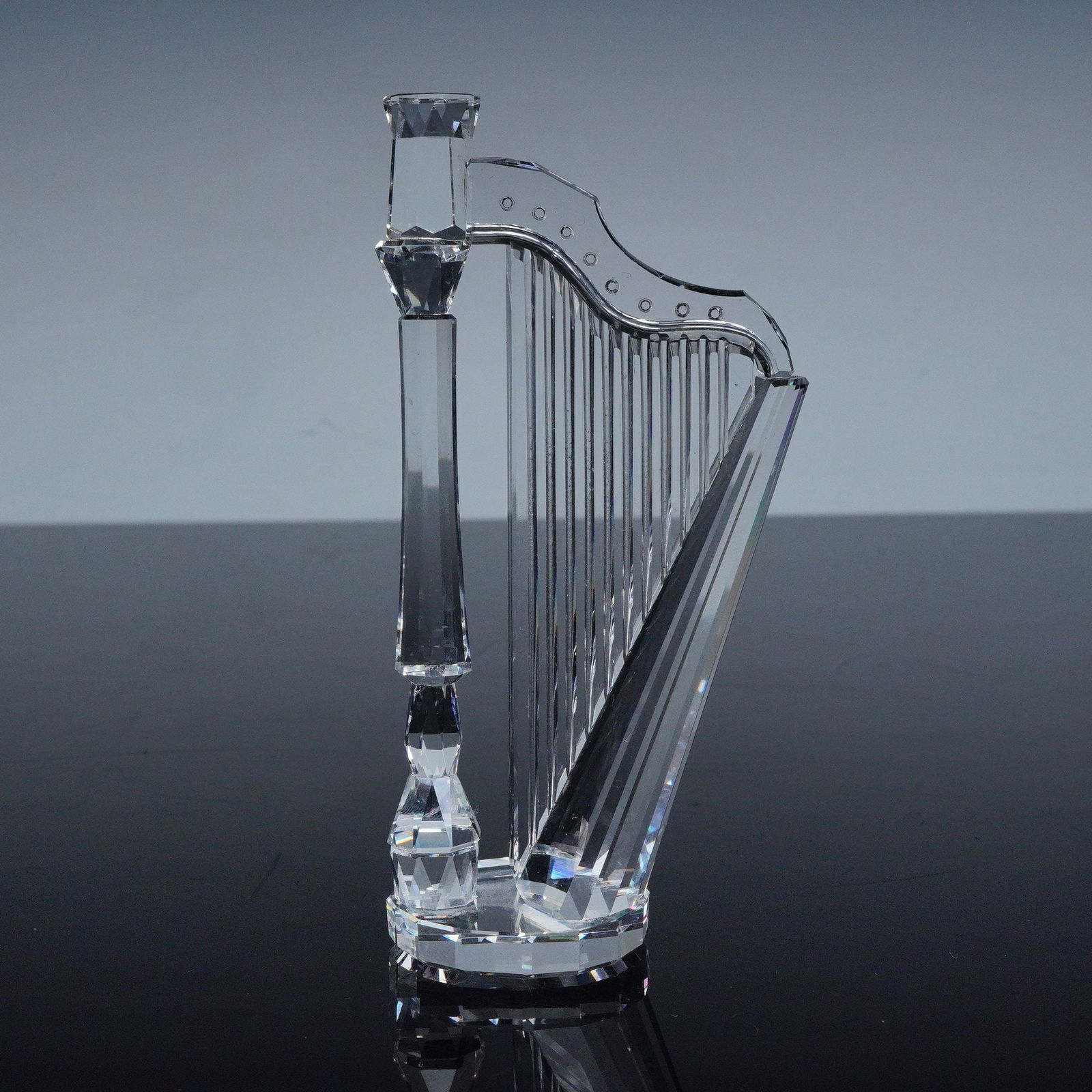 Swarovski Crystal Melodies Figurine, Harp: A finely crafted clear crystal figurine designed in the form of a harp, part of Swarovski's Crystal Melodies collection. The piece features precision-cut facets that beautifully capture and reflect li