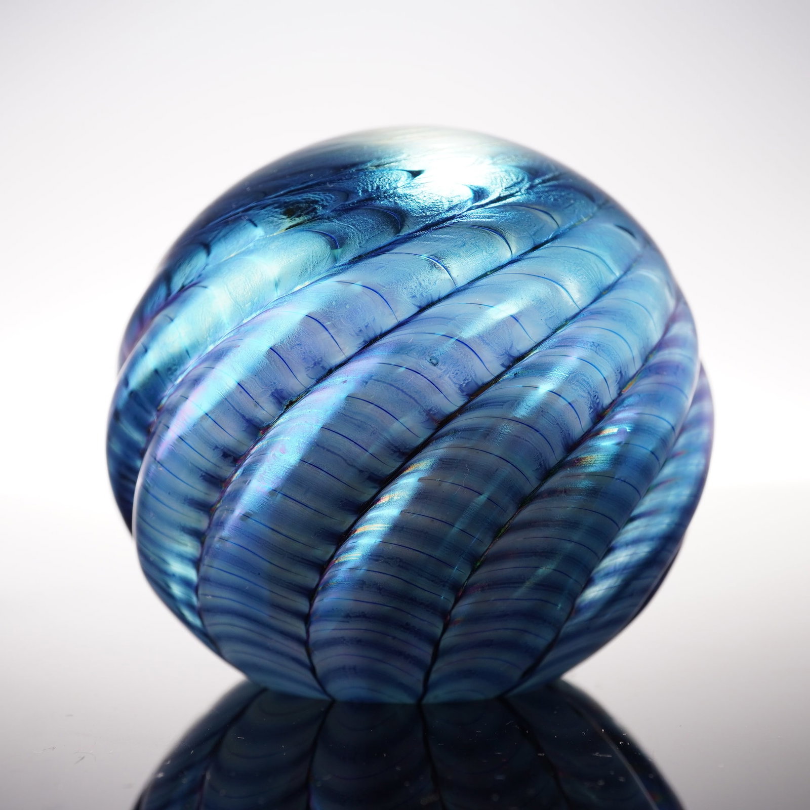 Studio Glass Paperweight, Blue Iridescent Swirl Design: A hand-blown studio glass paperweight of spherical form featuring a striking blue iridescent finish with spiral ribbed decoration encircling the body. The glass exhibits a vivid play of color when vie