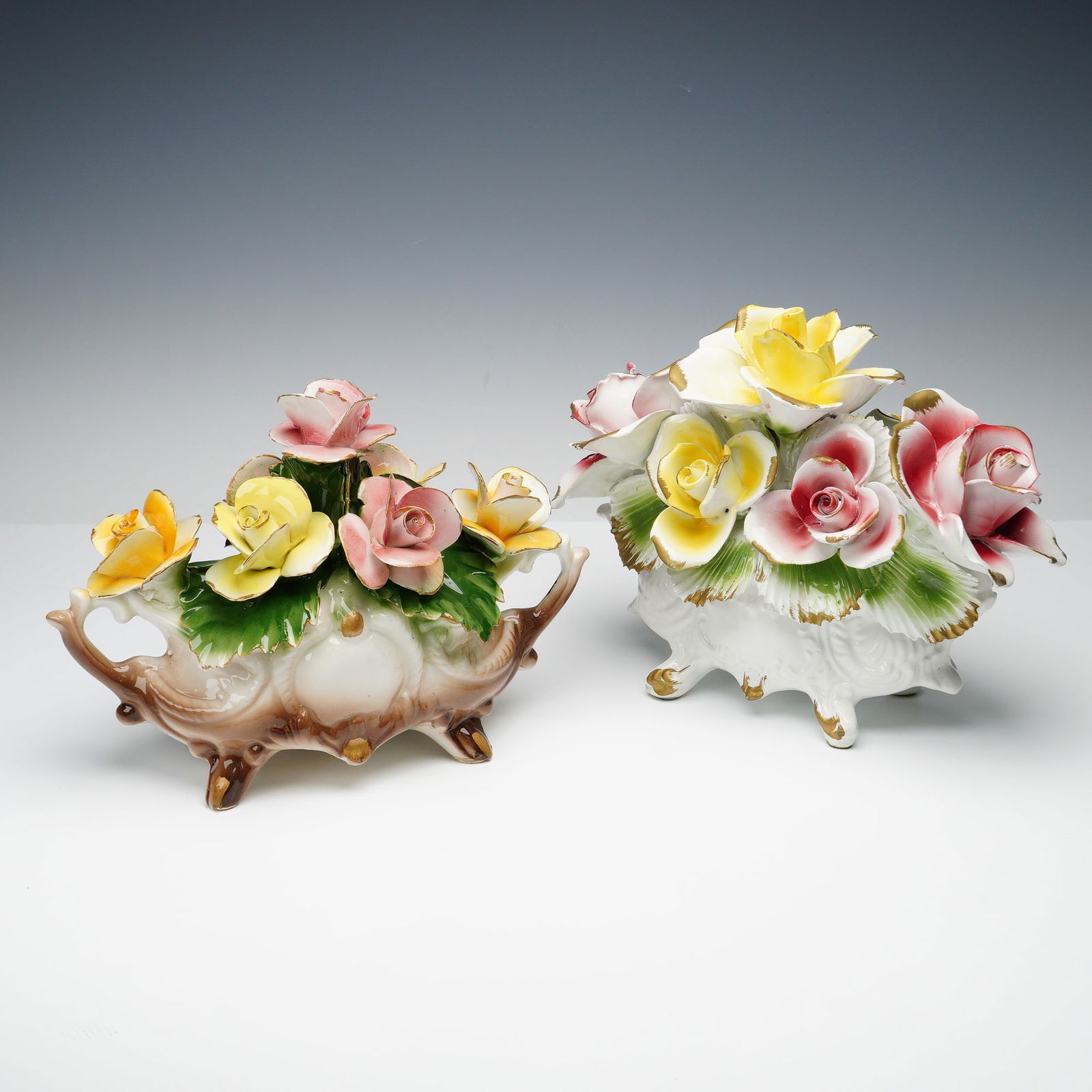2pc Nuova Capodimonte & Capodimonte Gilt Floral Centerpieces: Exquisite hand-painted porcelain floral arrangements featuring vividly colored roses in hues of yellow, pink, and white with delicate gilt edges. Each centerpiece displays intricate detailing and high