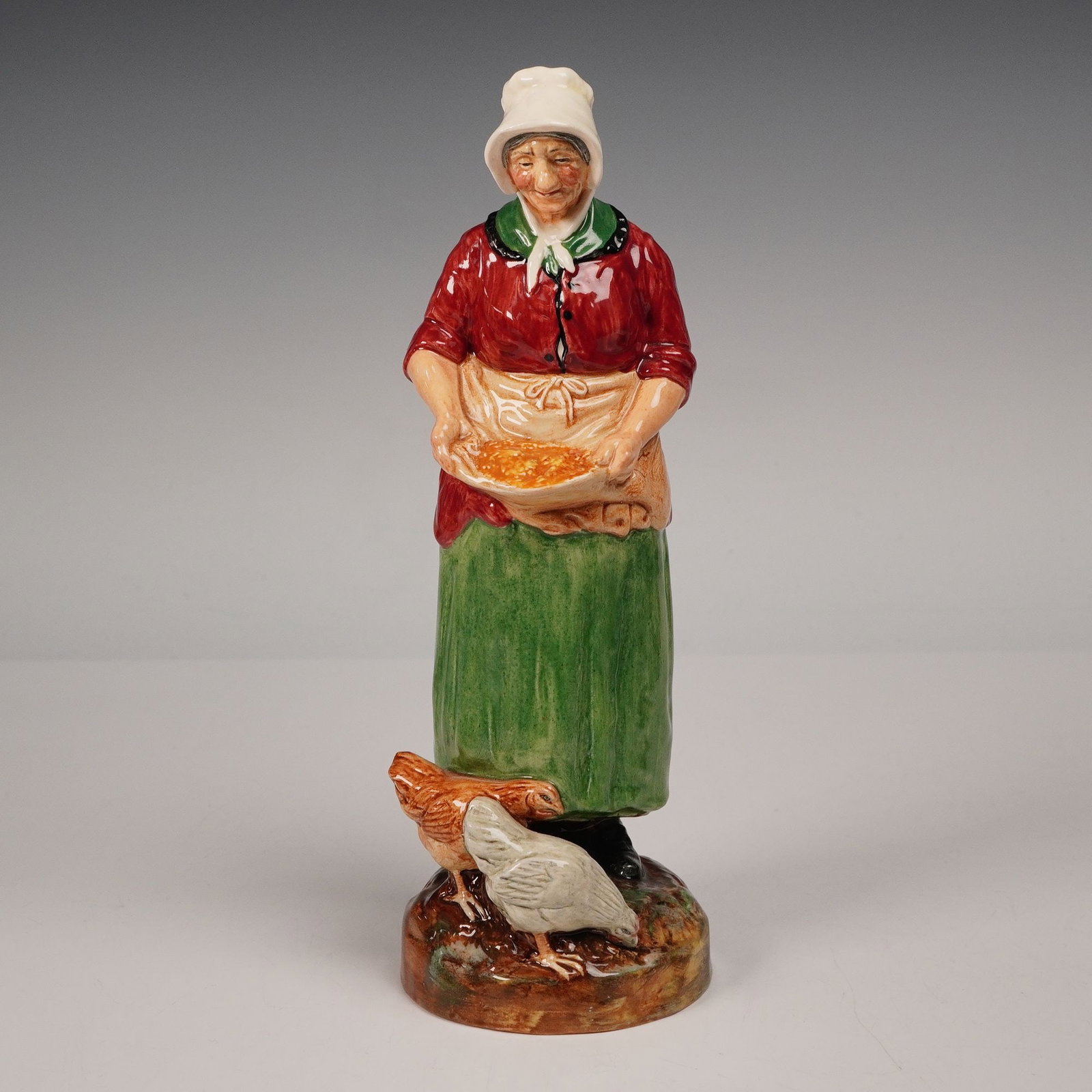 Royal Doulton Figurine, Farmers Wife HN2069: Figurine titled Farmer's Wife HN2069, designed by Leslie Harradine and issued in 1950 as part of the Farm & Country series. This charming piece depicts a cheerful farm woman wearing a red blouse, gree