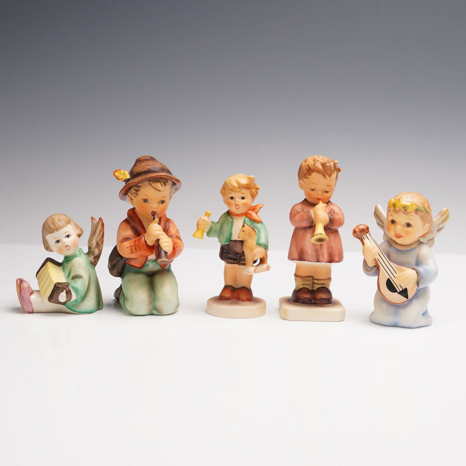 5pc Goebel Hummel Musical Figurines: Five porcelain figurines, each depicting children or angels playing musical instruments. Includes: Angel with accordion (233/B), Little Tooter (214/H/I), Boy with horse and horn (239), A Budding Maest
