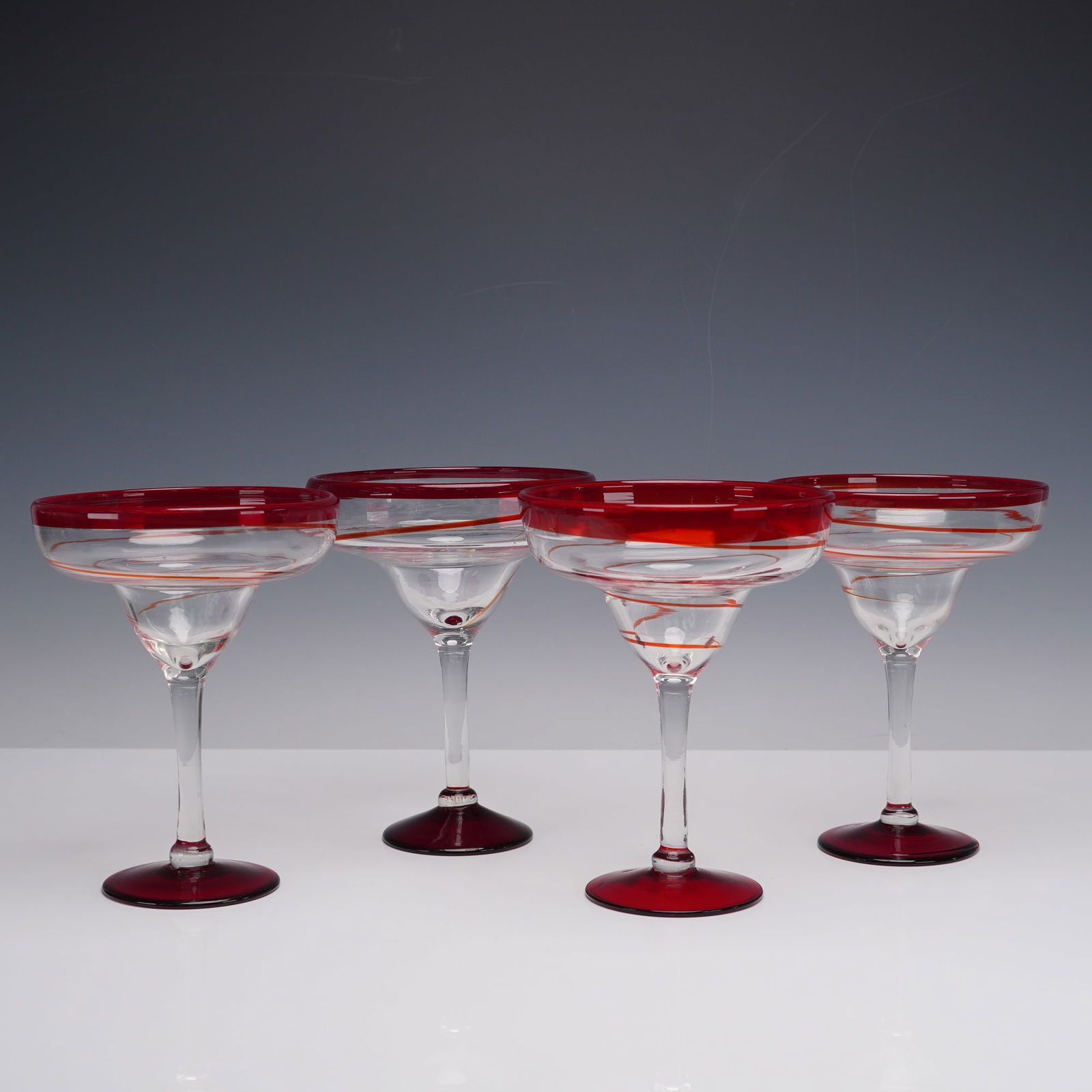 4pc TGI Friday's Red Swirl Margarita Glasses: Each crafted in clear glass with bold red accents. The wide bowls are decorated with a vivid red rim and swirling red lines that spiral downward, complemented by solid red bases. The stems are clear,