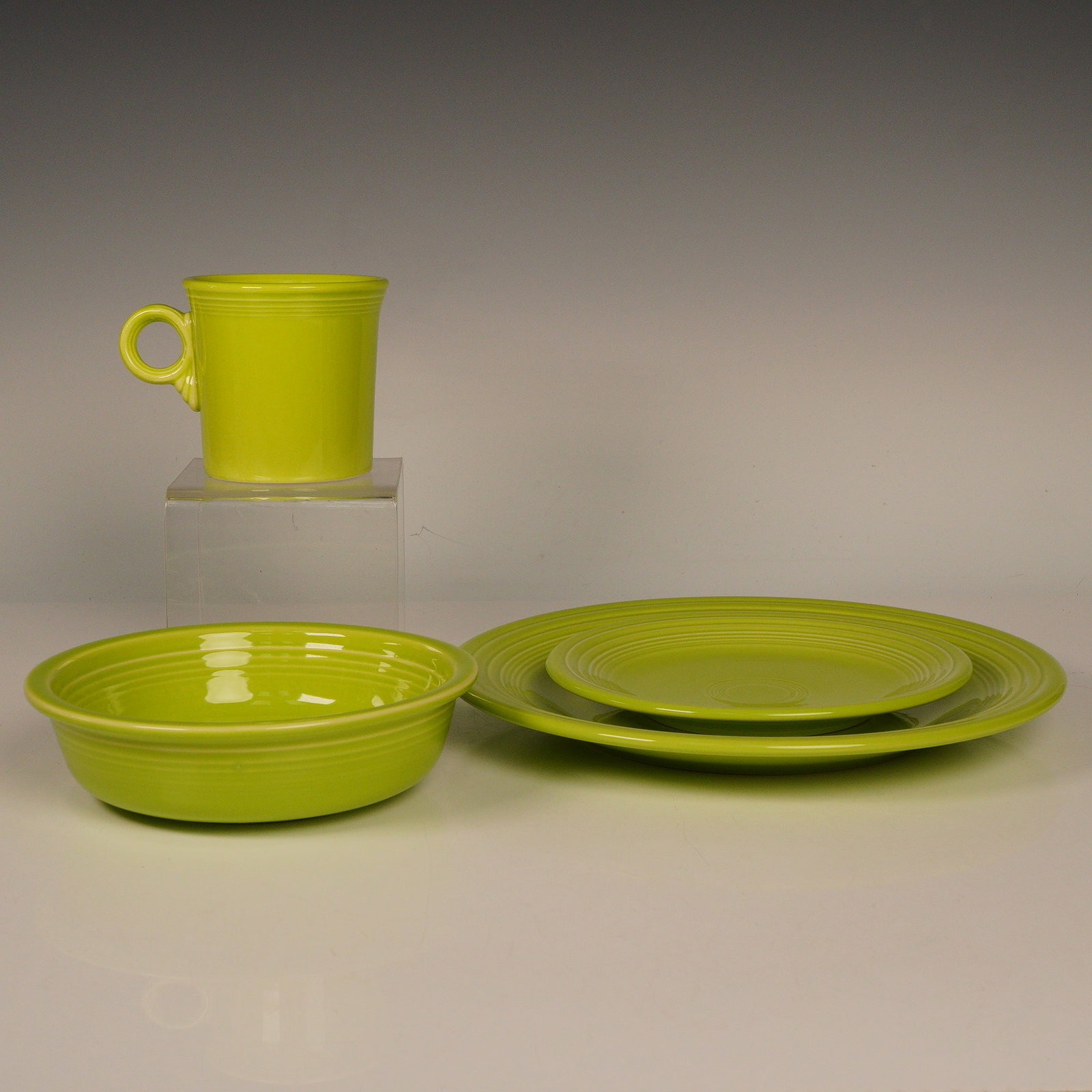 4pc Homer Laughlin China Fiestaware Set, Chartreuse: Offered here is a vibrant four-piece ceramic dinnerware set, part of their iconic Fiesta line in the bold chartreuse glaze. The ensemble includes one dinner plate, one salad plate, one soup or cereal