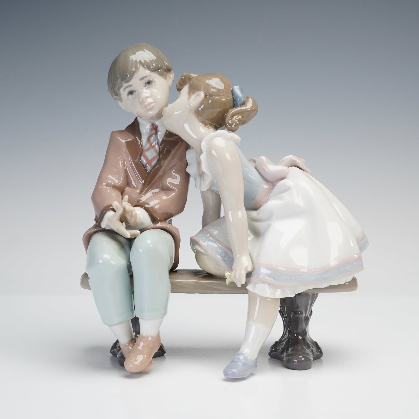 Lladro Porcelain Figurine, Ten and Growing 1007635: Lladro porcelain figurine titled Ten and Growing, sculpted by Francisco Polope. Depicts a young boy seated on a bench receiving a kiss from a girl. Issued in 1995 and retired the same year. Marked wit