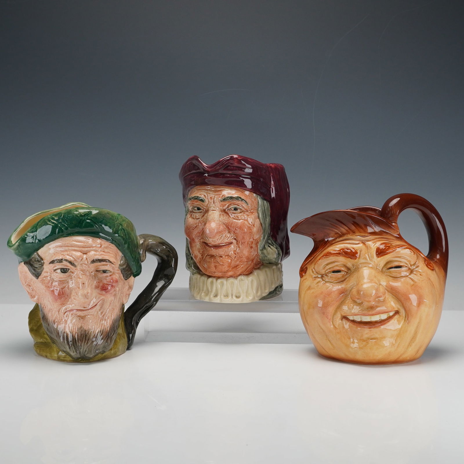 3pc Royal Doulton Large Character Jugs- D5823, D5504 & D5327: Royal Doulton large character jugs including Auld Mac D5823, depicting a bearded Scottish man wearing a green tam; Simon the Cellarer D5504, showing the jovial 16th-century innkeeper with a maroon cap