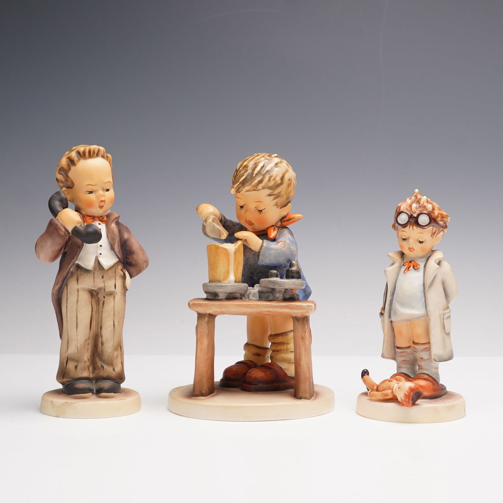 3pc Goebel Hummel Figurines: This charming trio of Hummel figurines is full of playful character and detail. Hello features a boy dressed smartly as he holds a telephone with a lively expression. The Doctor shows a young boy in a
