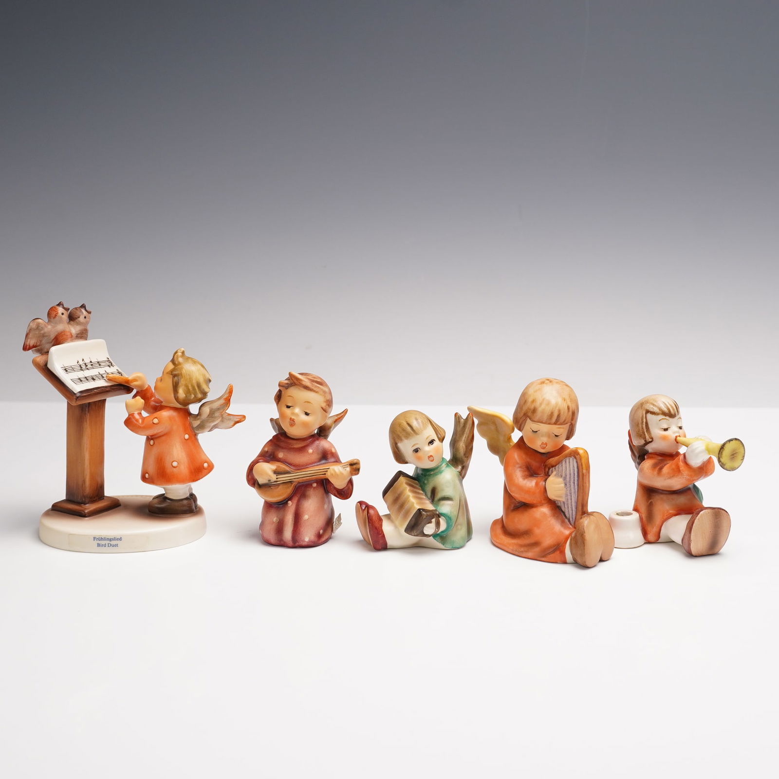 5pc Goebel Hummel Musical Angel Figurines: A graceful set of five Goebel Hummel porcelain figurines of angels making music. Included are an angel at a music stand with birds, one with mandolin, one with accordion, one with harp, and one blowin