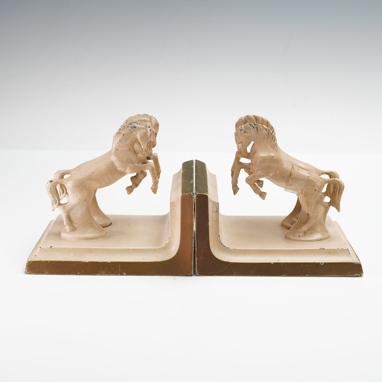 Pair of Cast Metal Horse Bookends: Pair of vintage cast metal bookends featuring rearing horses in matching pose, mounted on rectangular bases with stepped edges. Finished in a light cream toned paint. Issued: 20th century Dimensions: 