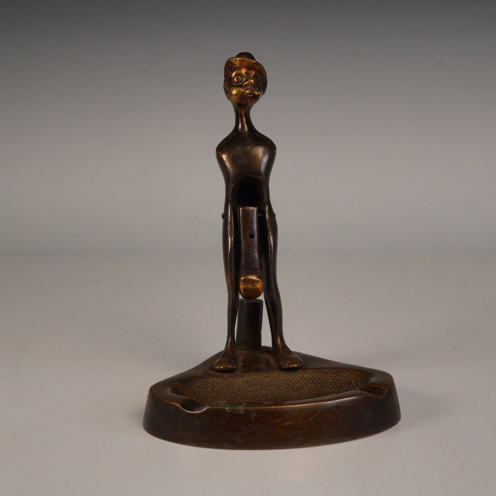 Figural Bronze Ashtray with Standing Man Form: Whimsical cast bronze figural ashtray featuring a stylized standing man wearing a hat, posed beside an integrated circular tray. The minimalist elongated design exhibits fine mid-century character wit