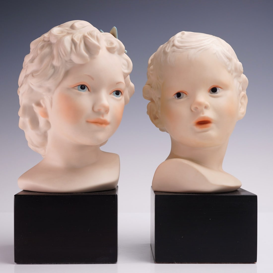 2pc Cybis Porcelain Busts of Children Mounted on Bases: Pair of sculpted busts of children signed Cybis, each modeled in bisque porcelain or ceramic and permanently affixed to square wood bases. These heads are detailed with soft features and delicately pa