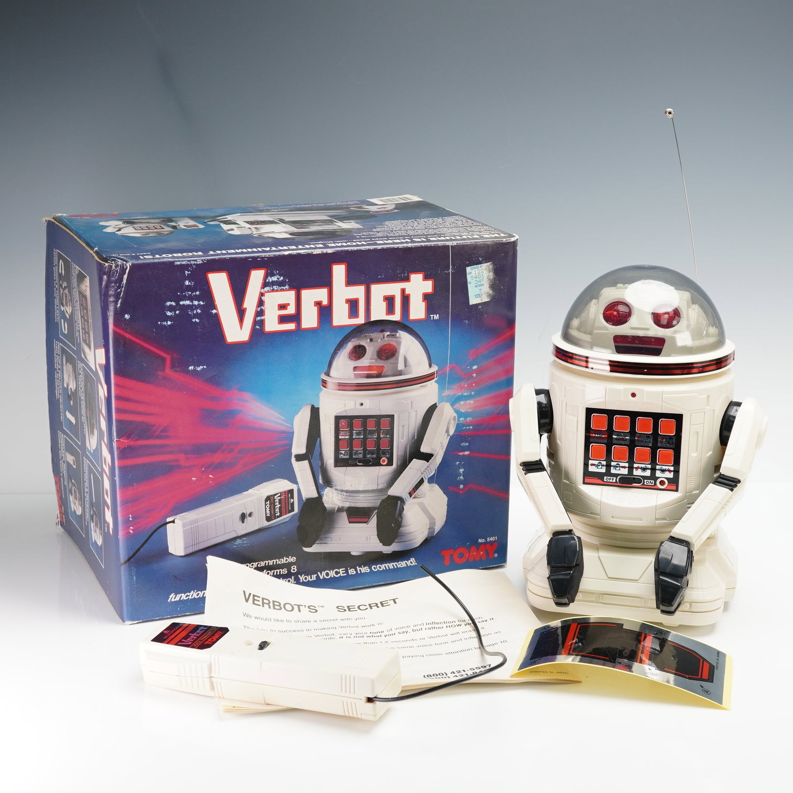 Tomy Corp. Voice-Command Toy Robot, 5401 Verbot RX: The robot features a white plastic body with black and red accents, a clear dome head with visible internal components, red light-up eyes, and a front control panel with red command buttons. It includ